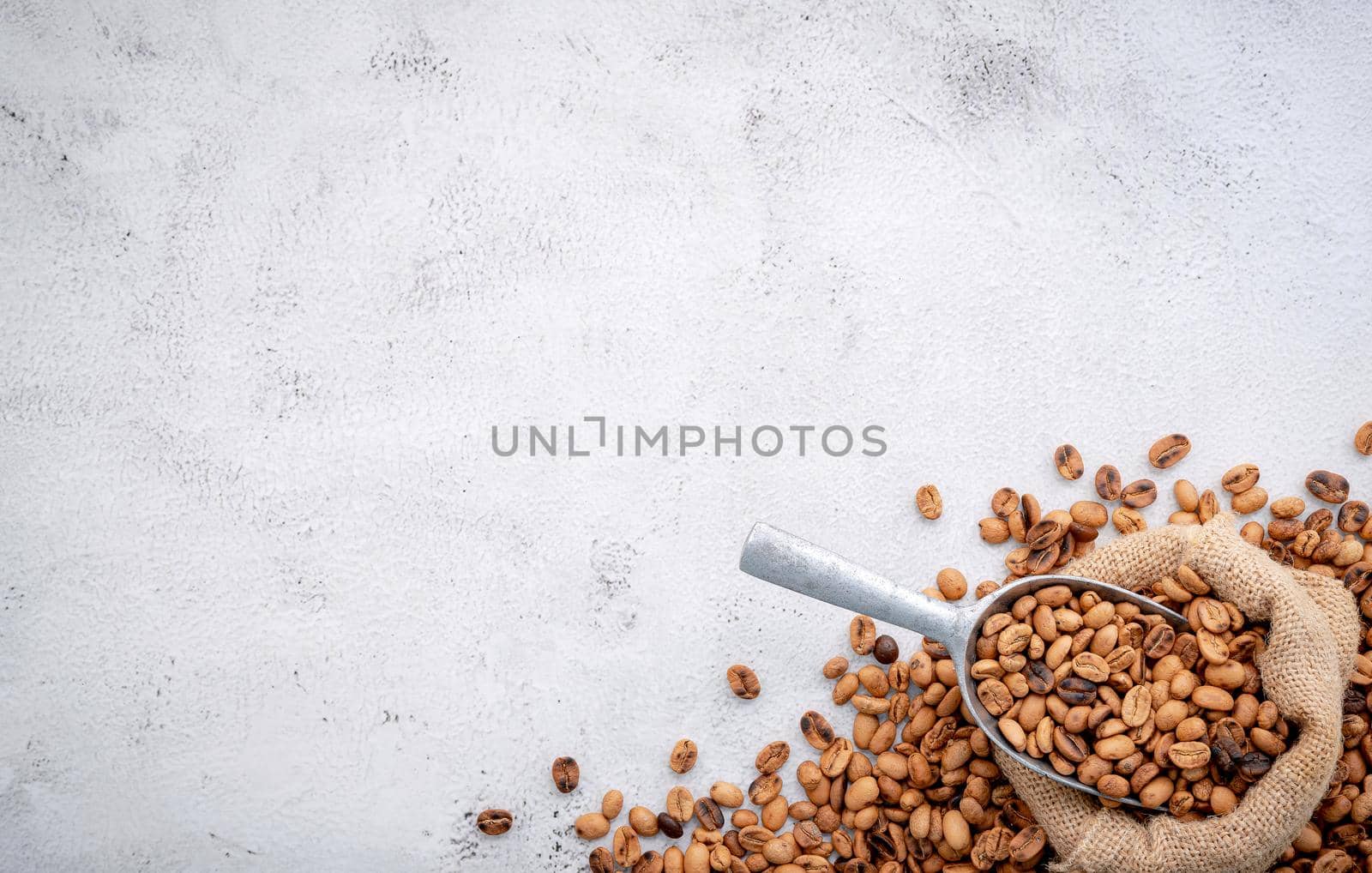 Roasted coffee beans with scoops setup on white concrete background.