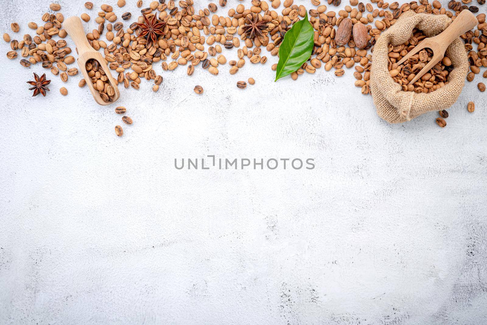 Roasted coffee beans with scoops setup on white concrete background.