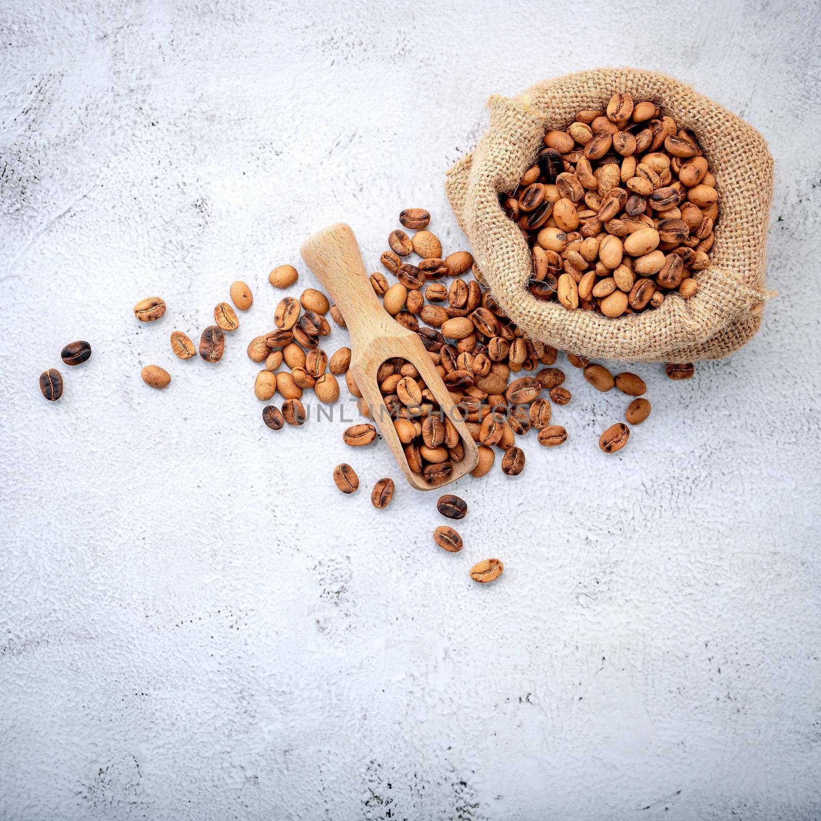 Roasted coffee beans with scoops setup on white concrete background.