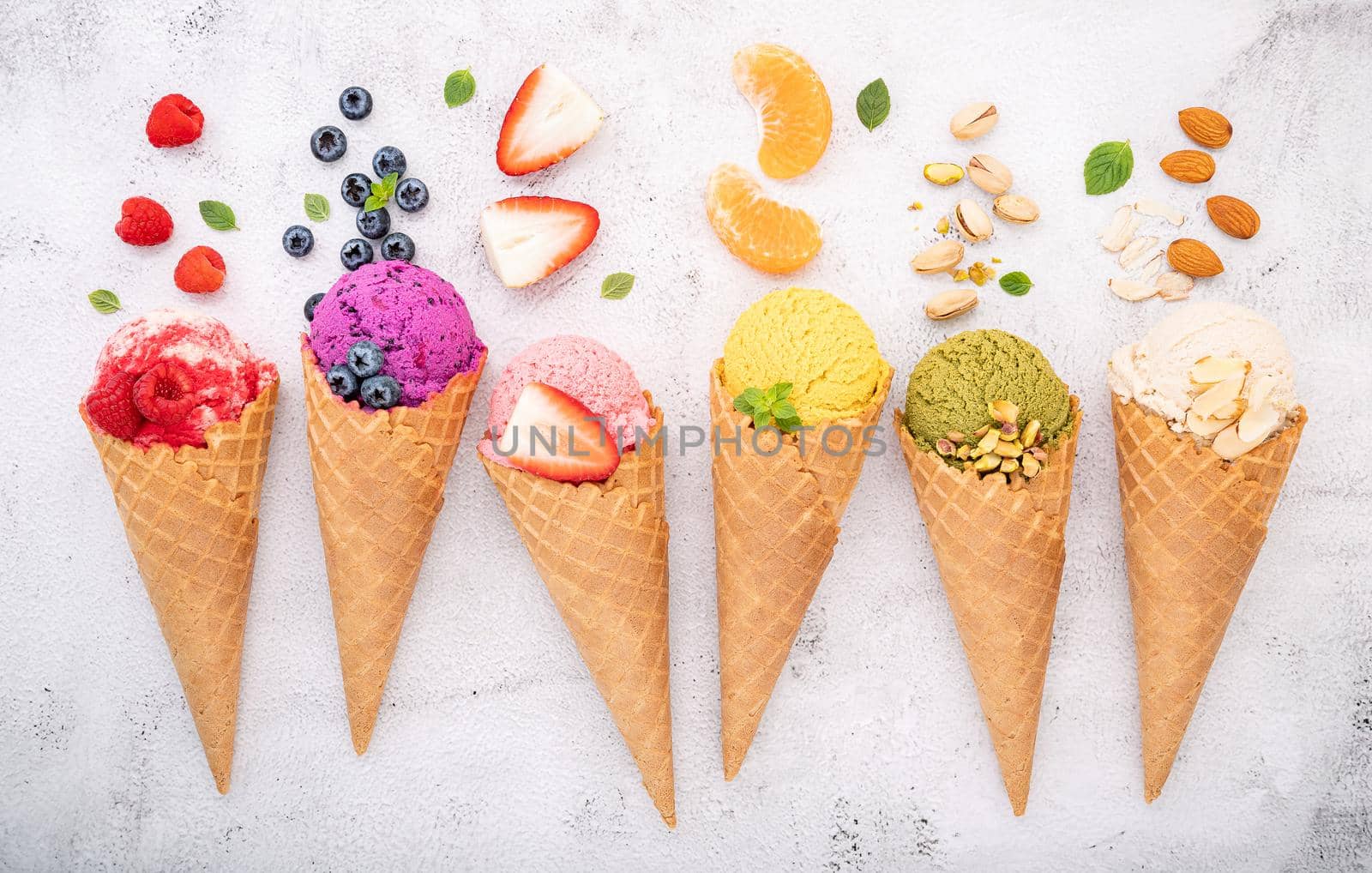 Various of ice cream flavor in cones blueberry ,pistachio ,almond ,orange and cherry setup on white stone background . Summer and Sweet menu concept.