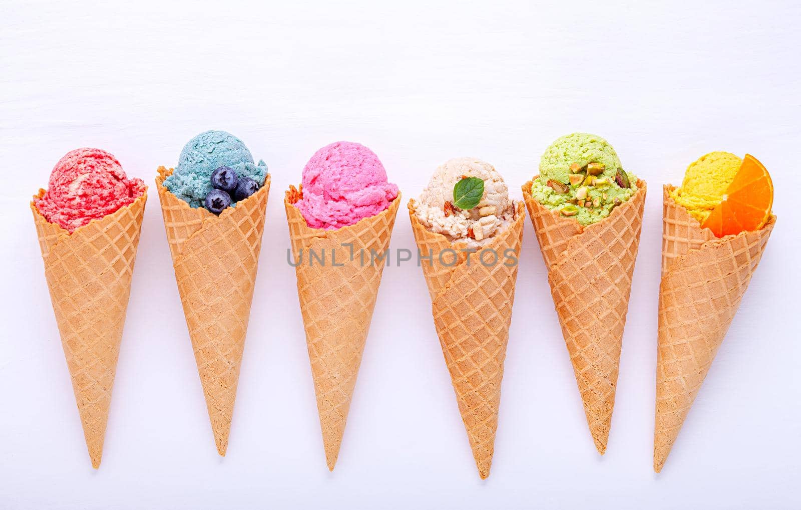 Various of ice cream flavor in cones blueberry ,strawberry ,pistachio ,almond ,orange and cherry setup on white wooden background . Summer and Sweet menu concept.