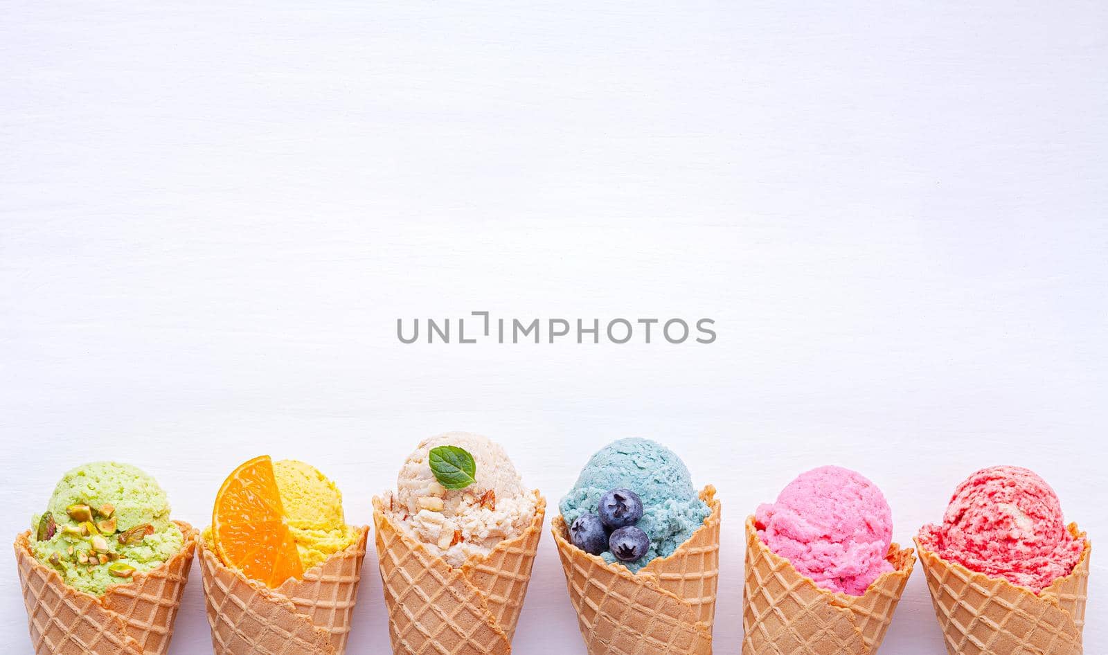 Various of ice cream flavor in cones blueberry ,strawberry ,pistachio ,almond ,orange and cherry setup on white wooden background . Summer and Sweet menu concept.