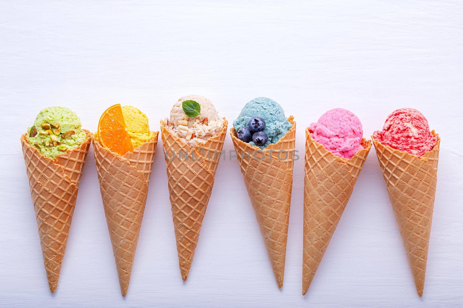 Various of ice cream flavor in cones blueberry ,strawberry ,pistachio ,almond ,orange and cherry setup on white wooden background . Summer and Sweet menu concept. by kerdkanno