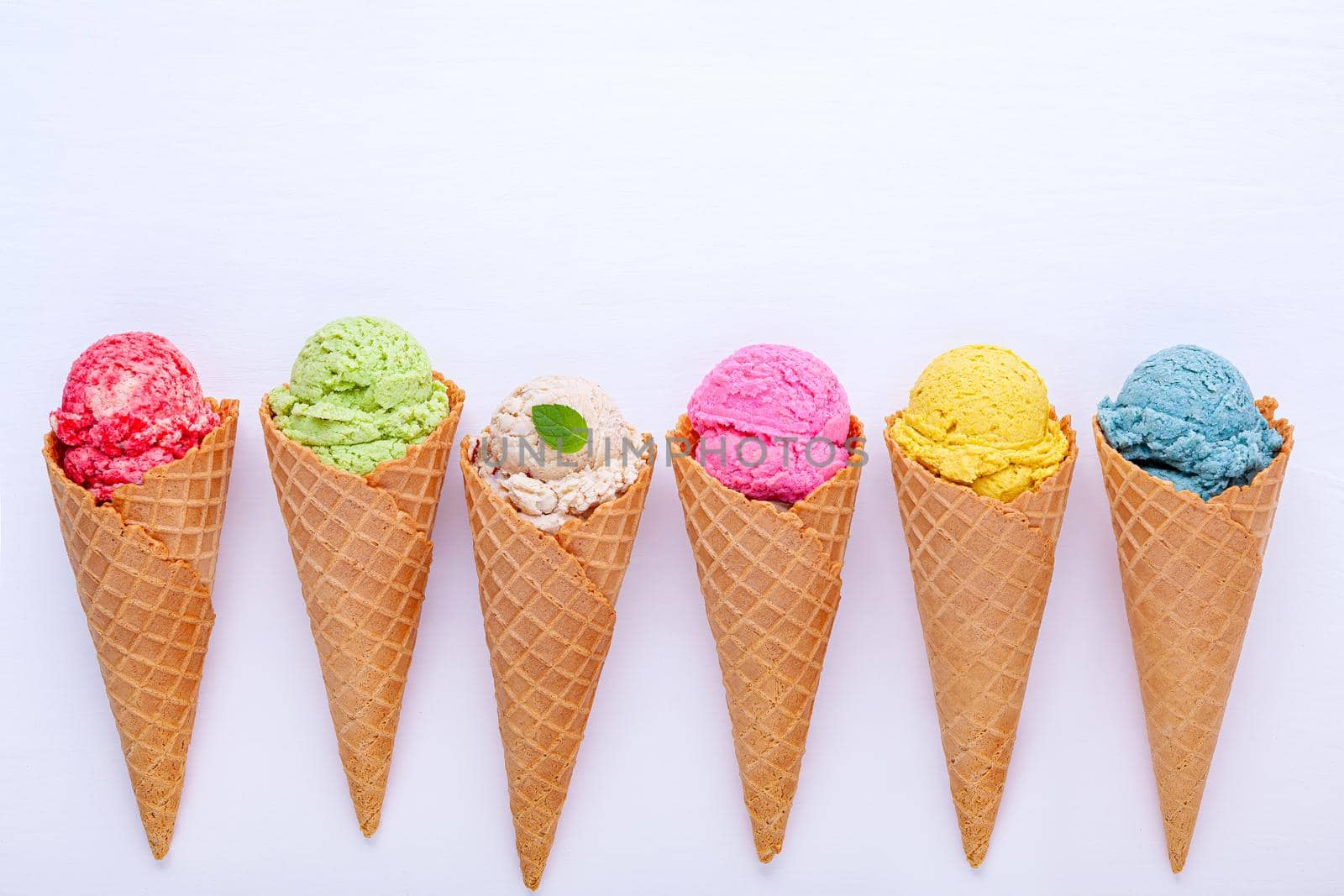 Various of ice cream flavor in cones blueberry ,strawberry ,pistachio ,almond ,orange and cherry setup on white wooden background . Summer and Sweet menu concept.