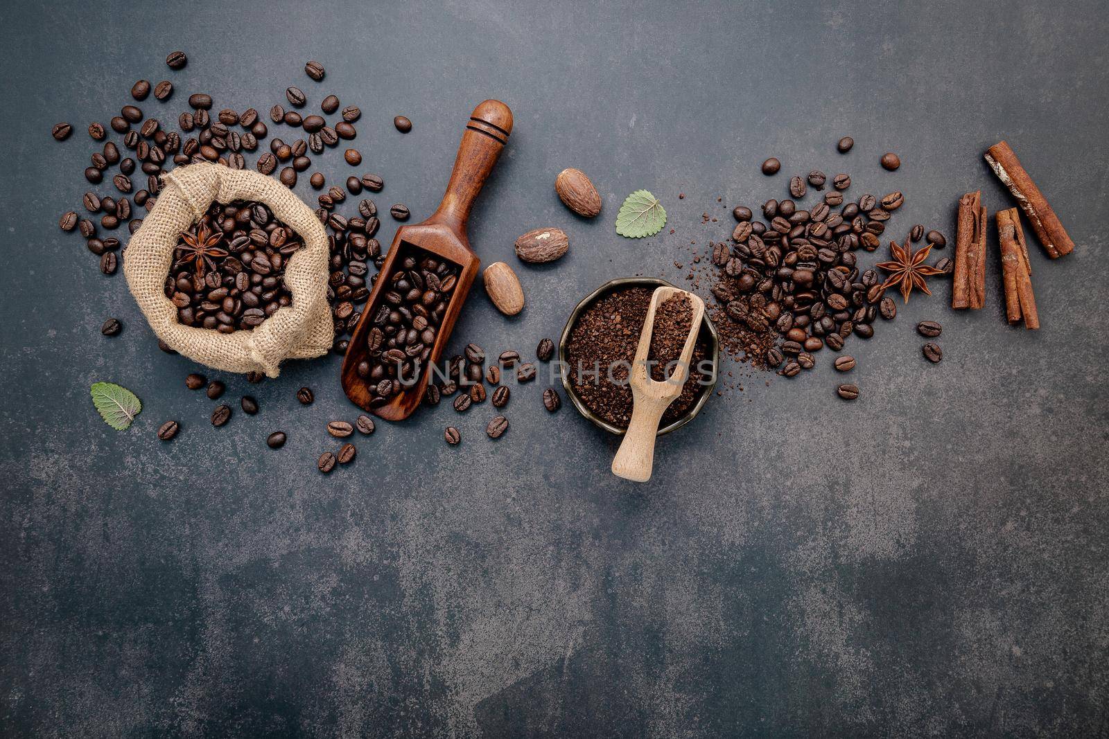 Roasted coffee beans with coffee powder and flavourful ingredients for make tasty coffee setup on dark stone background.