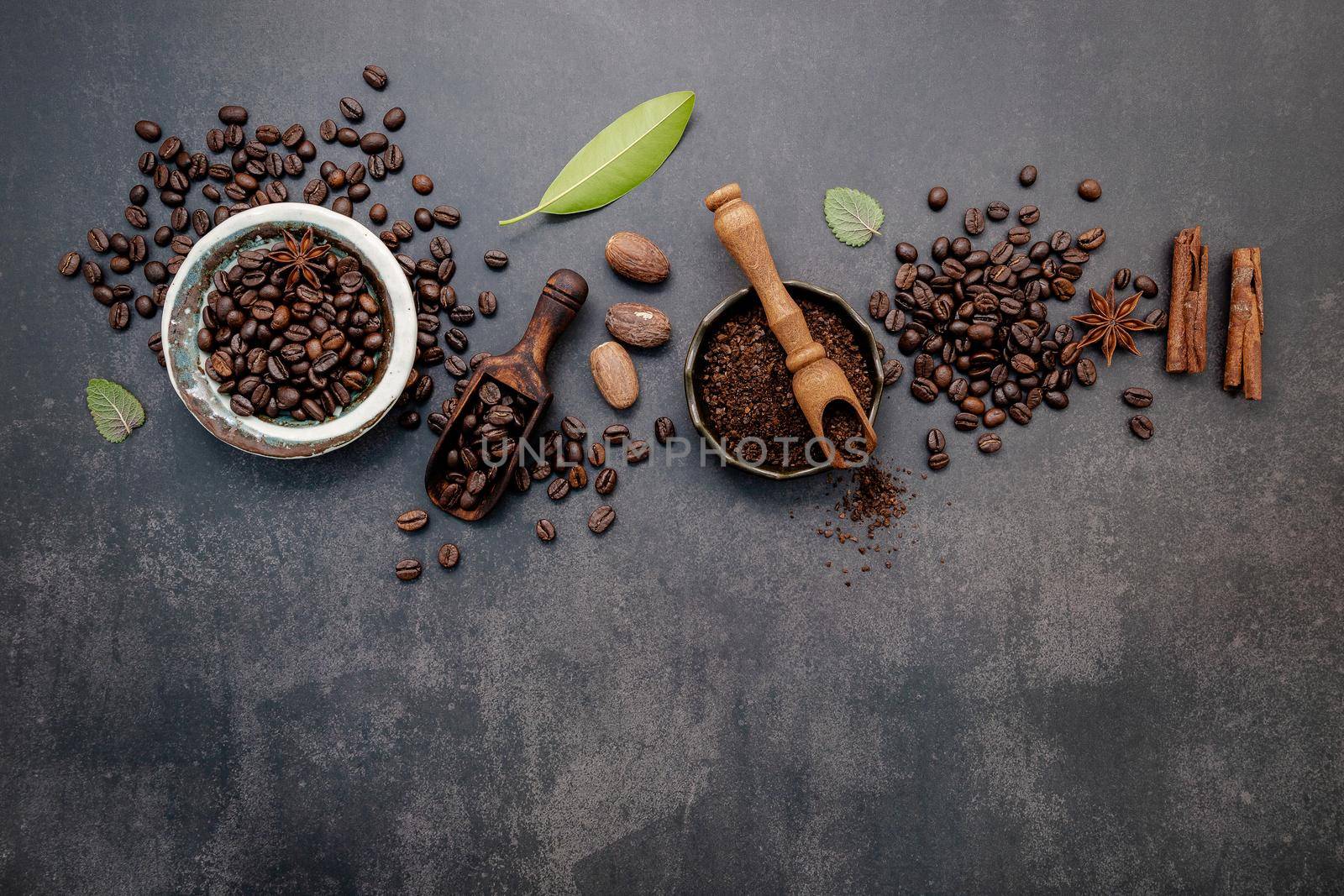 Roasted coffee beans with coffee powder and flavourful ingredients for make tasty coffee setup on dark stone background.