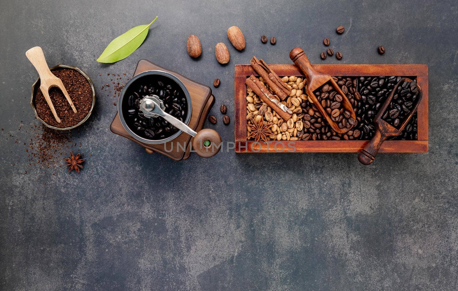 Various of roasted coffee beans in wooden box with manual coffee grinder setup on dark stone background.