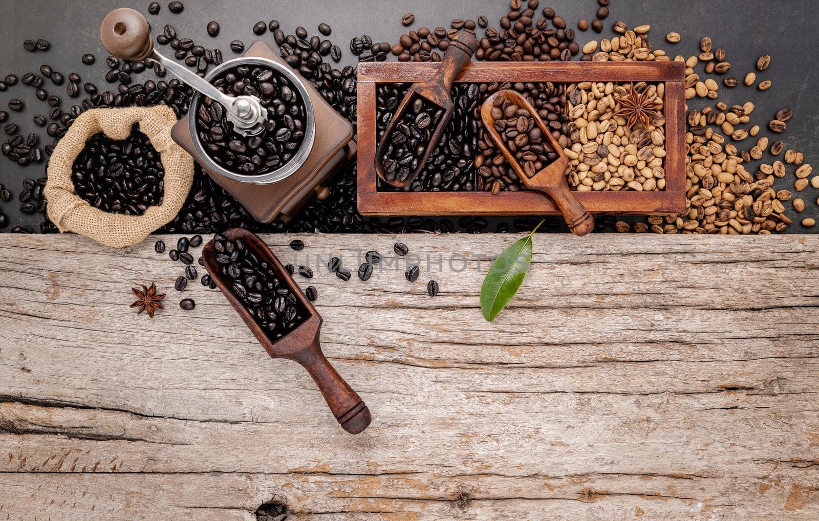 Various of roasted coffee beans in wooden box with manual coffee grinder setup on shabby wooden background.