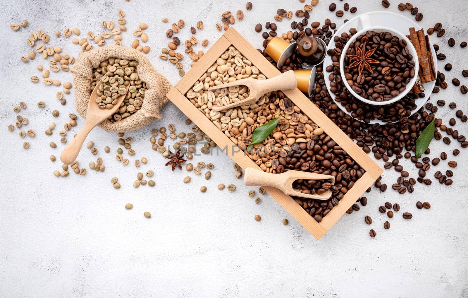 Green and brown decaf unroasted and dark roasted coffee beans in wooden box with scoops setup on white concrete background. by kerdkanno