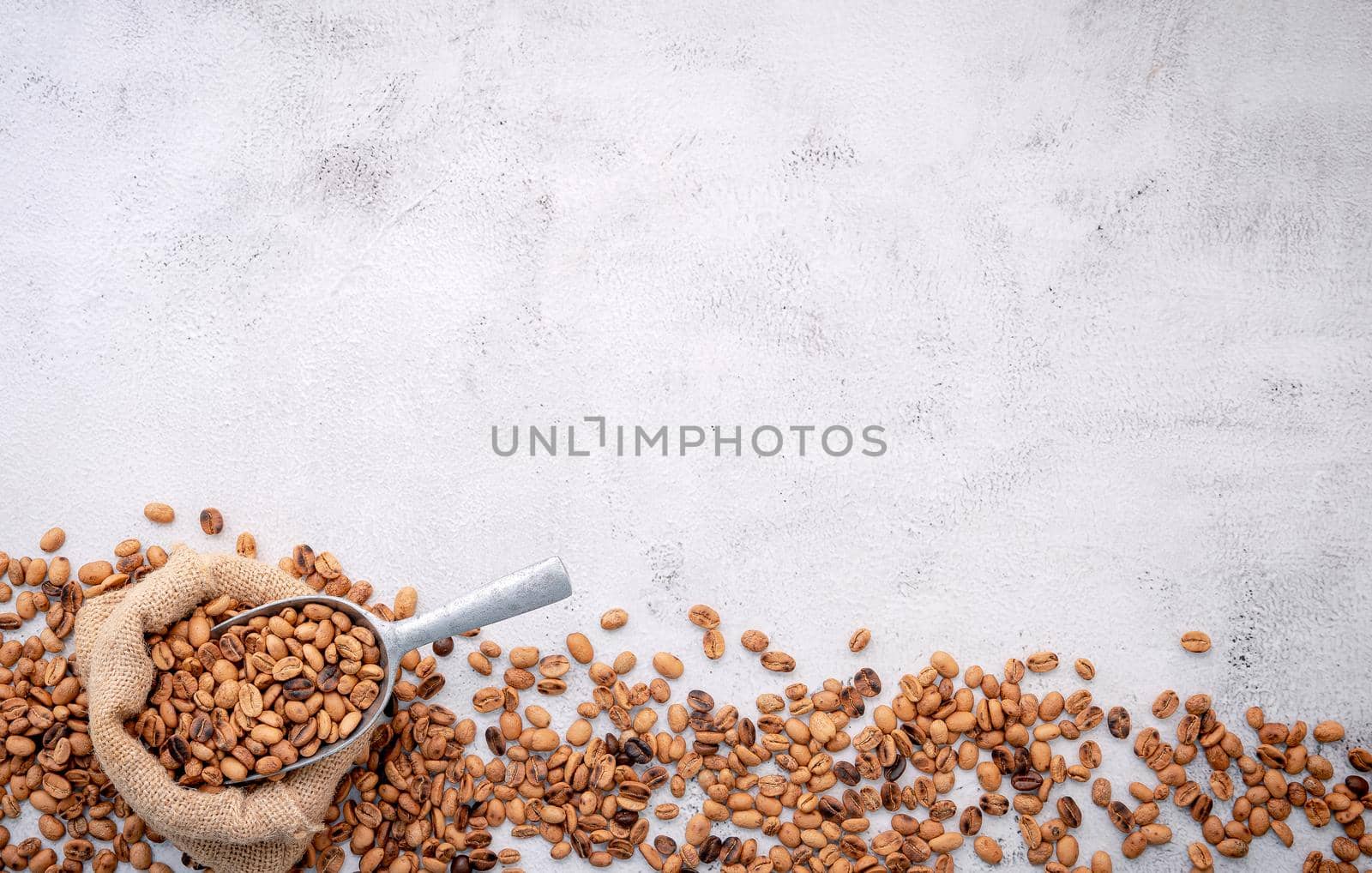 Roasted coffee beans with scoops setup on white concrete background.