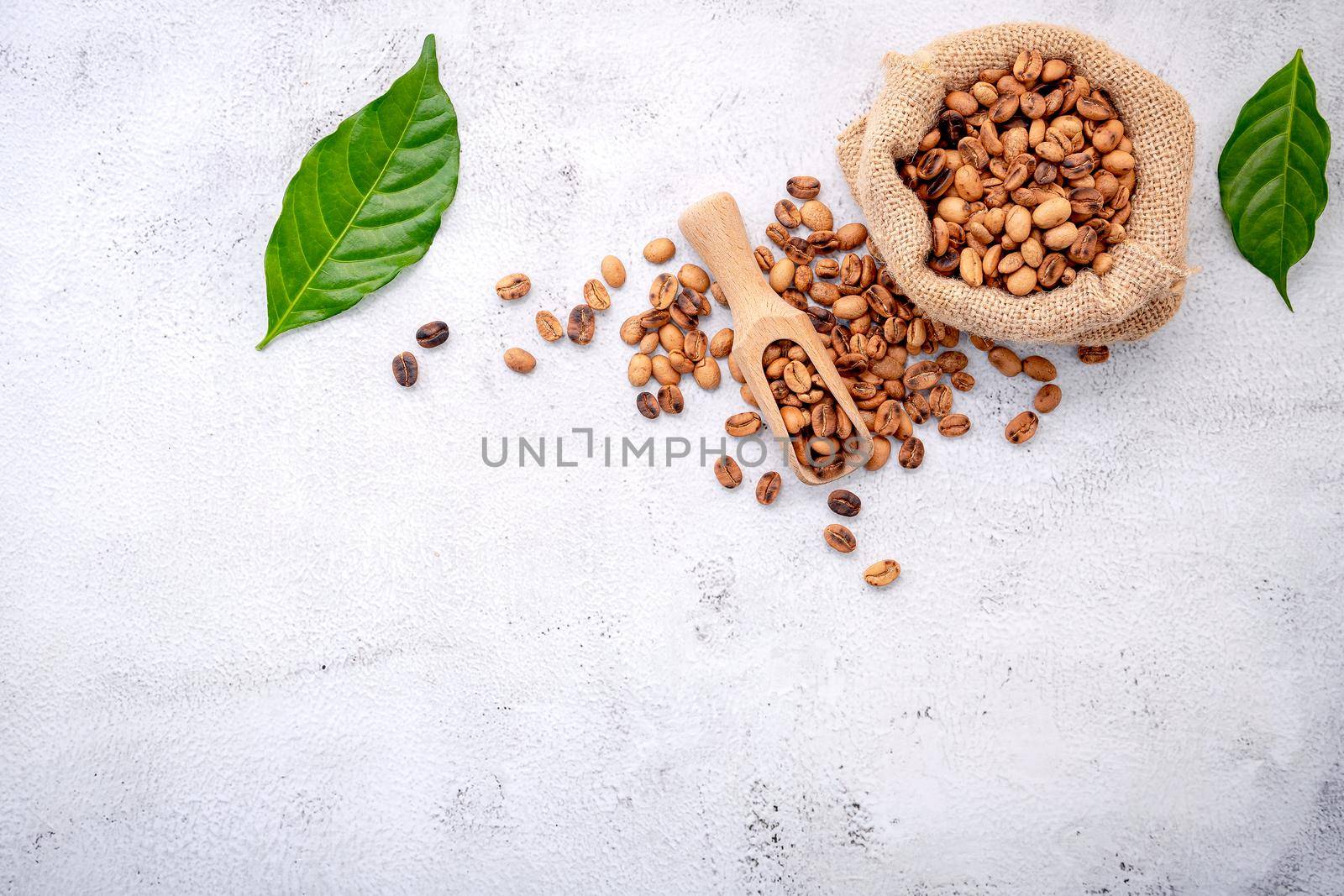 Roasted coffee beans with scoops setup on white concrete background.