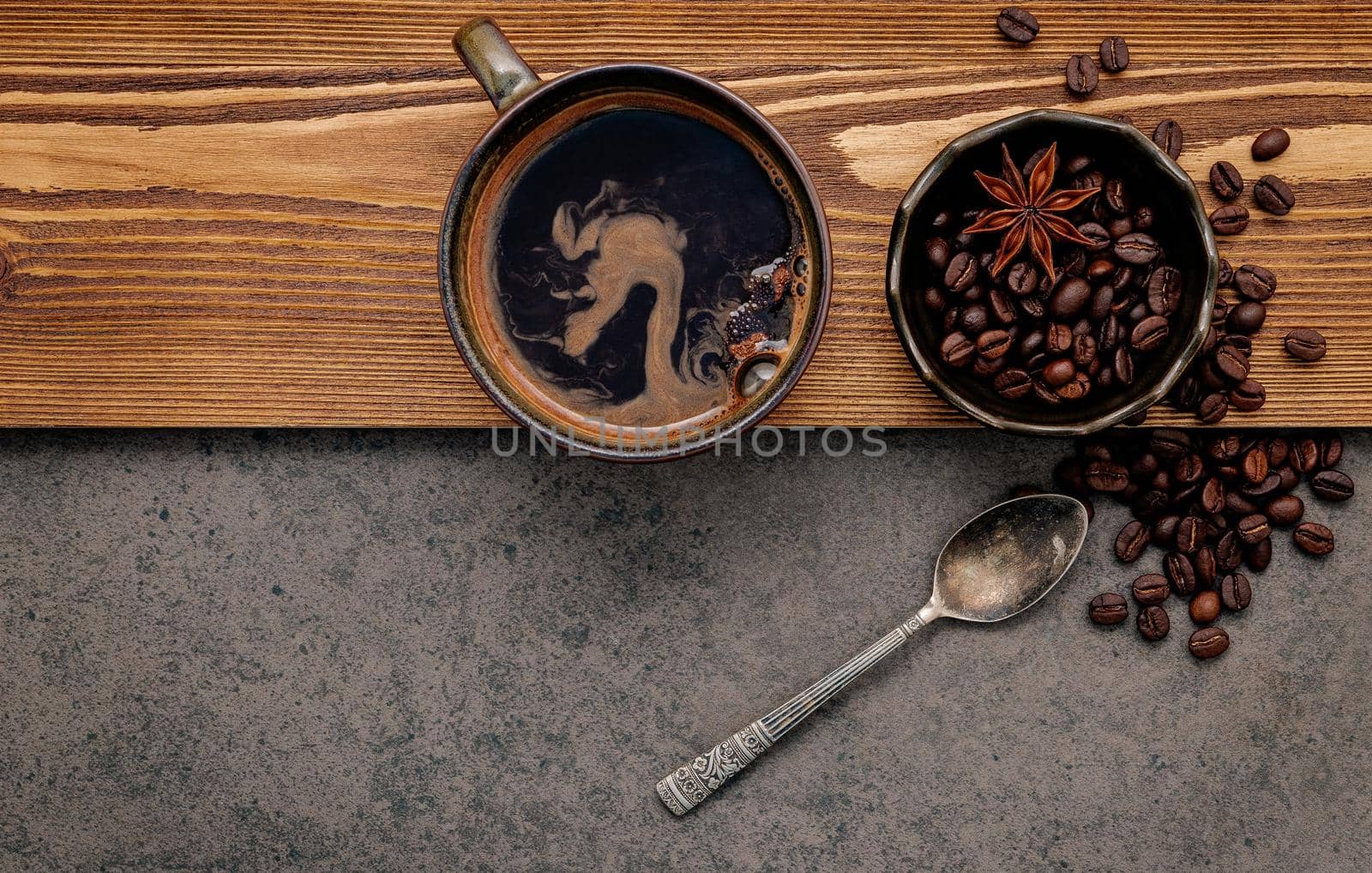 Roasted coffee beans with coffee cup setup on dark stone background.