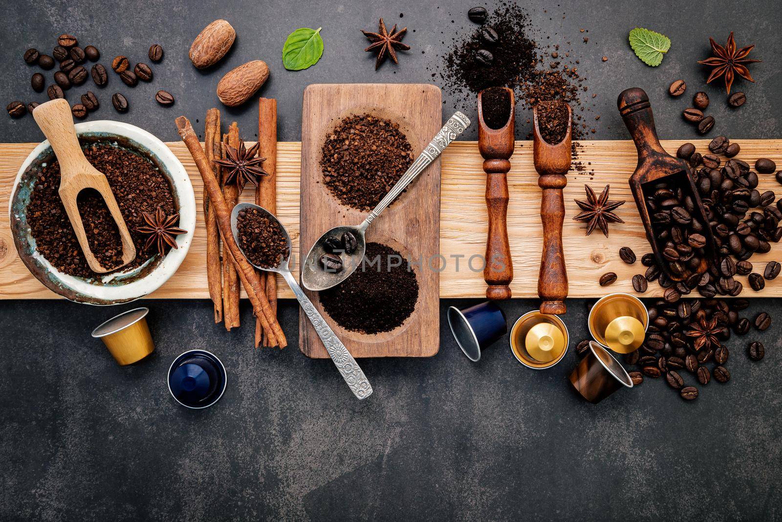 Roasted coffee beans with coffee powder and flavourful ingredients for make tasty coffee setup on dark stone background.