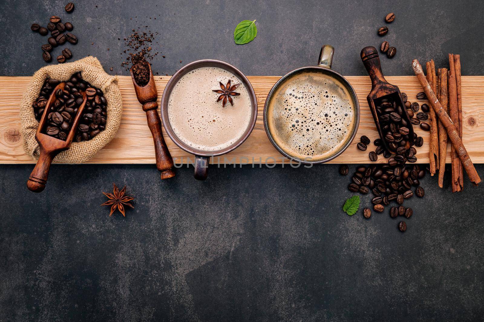 Roasted coffee beans with coffee powder and flavourful ingredients for make tasty coffee setup on dark stone background.