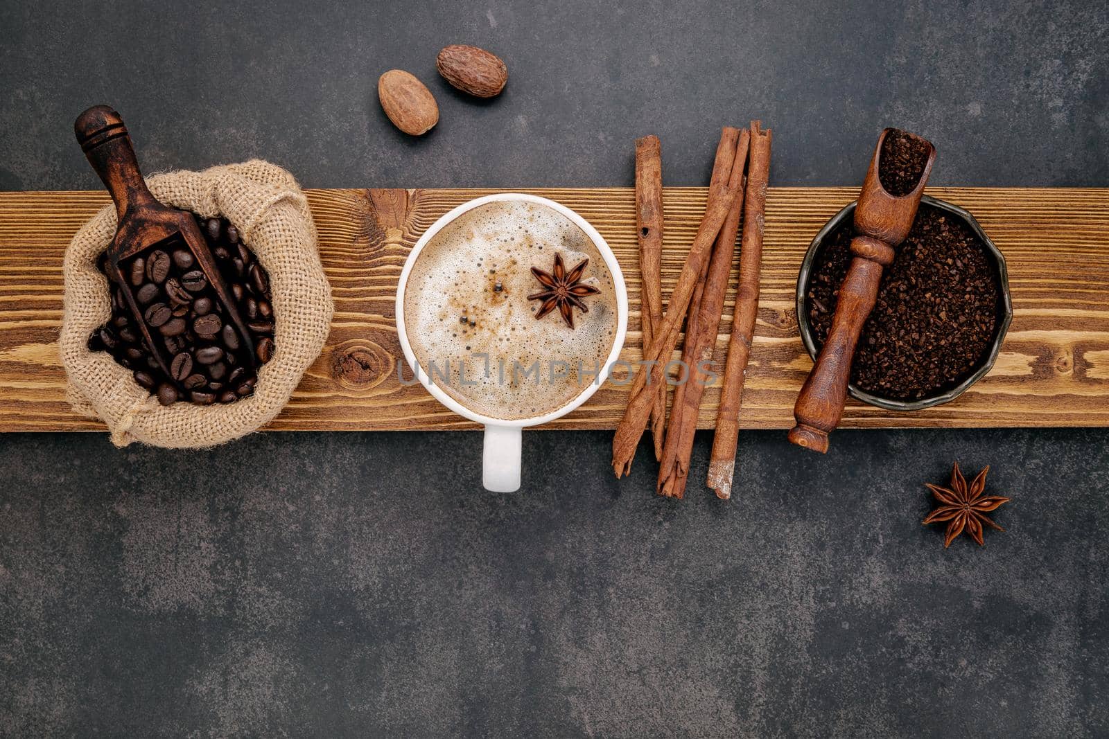 Cup of coffee and roasted coffee beans ,coffee powder and flavourful ingredients for make tasty coffee setup on dark stone background.