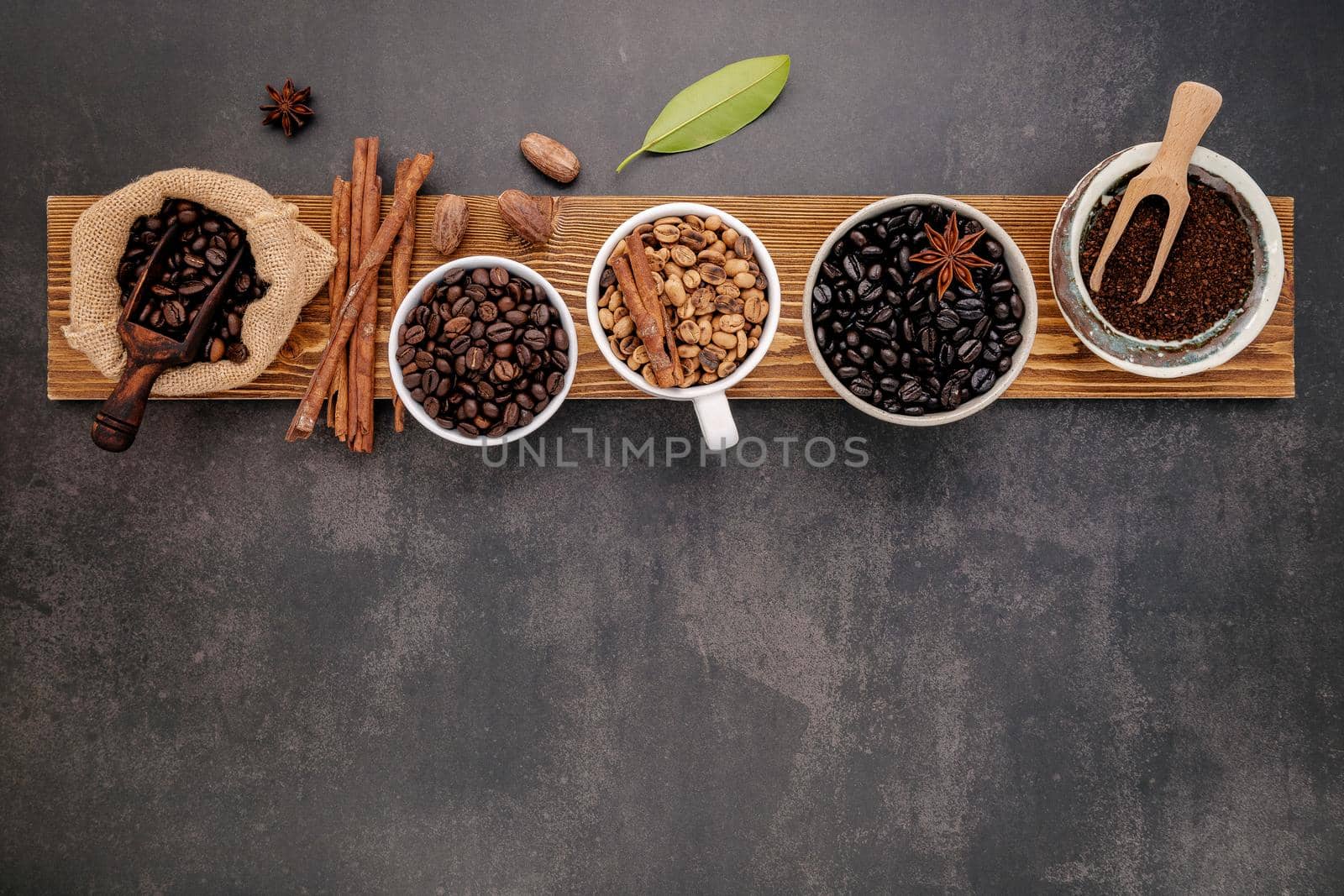 Brown unroasted and dark roasted coffee beans in coffee cup with scoops setup on dark stone background. by kerdkanno