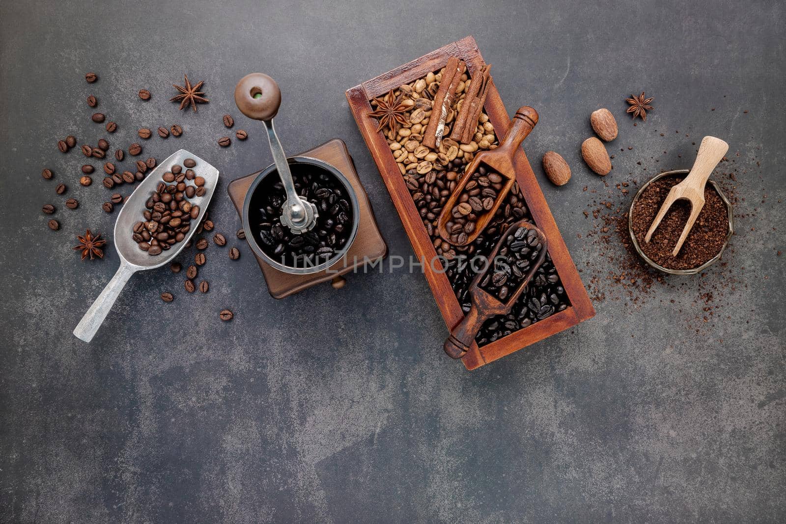 Various of roasted coffee beans in wooden box with manual coffee grinder setup on dark stone background.