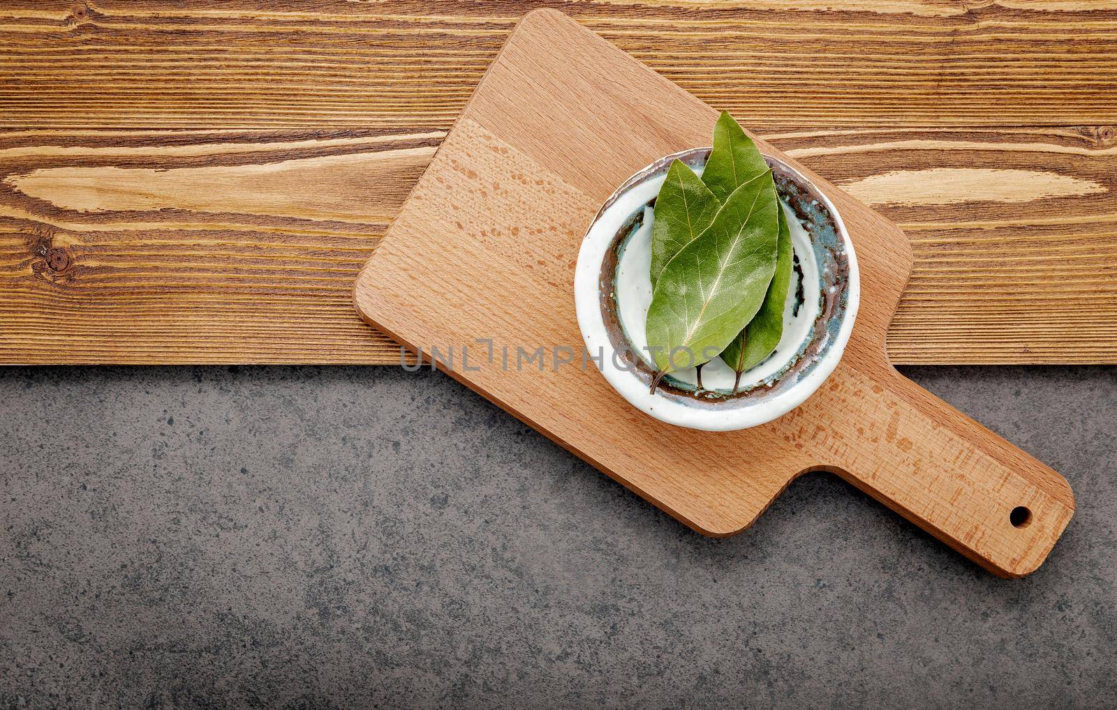 The bay leaves in ceramic bowl on shabby wooden background with copy space .