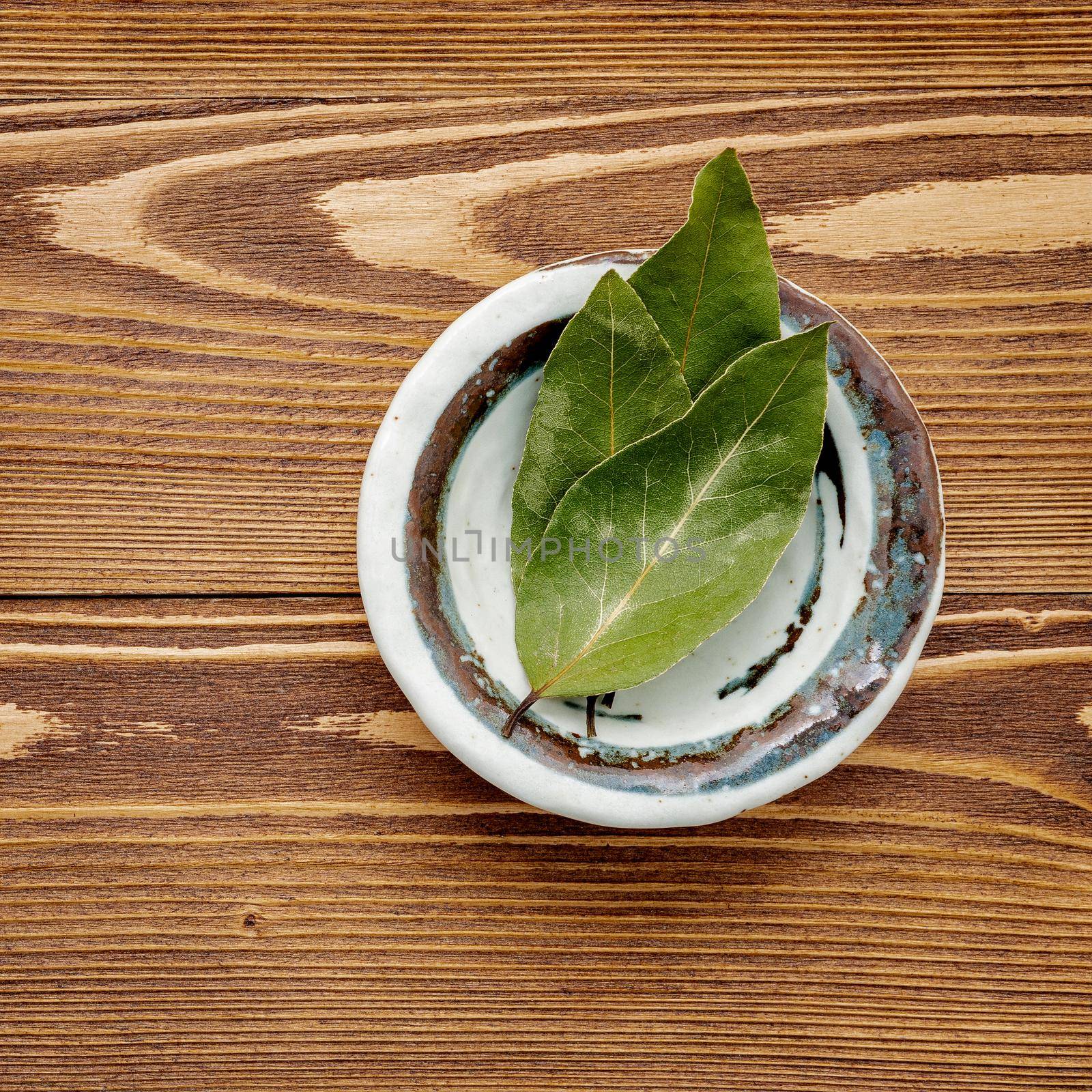 The bay leaves in ceramic bowl on shabby wooden background with copy space .