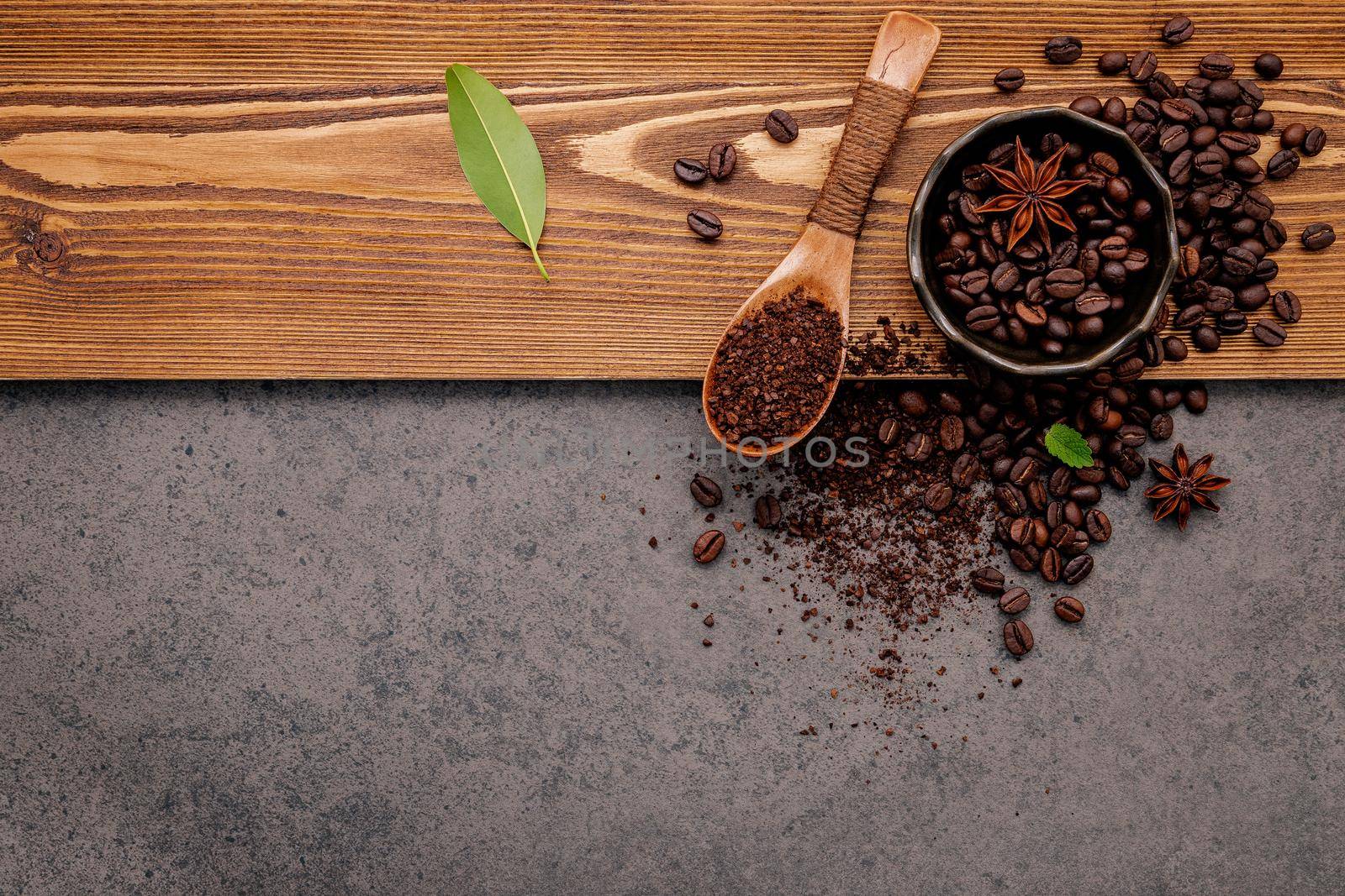 Roasted coffee beans with coffee powder setup on dark stone background.