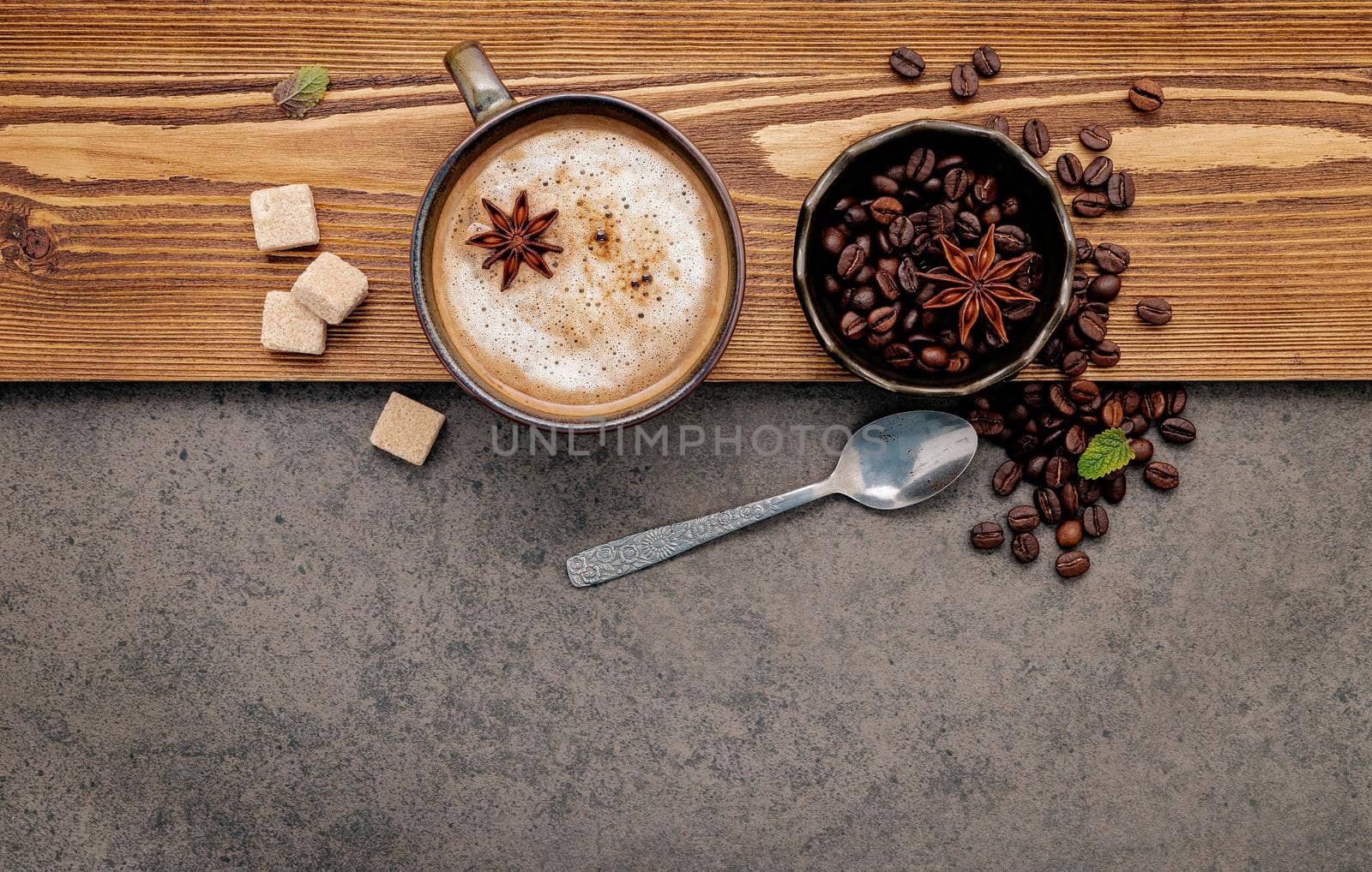 Roasted coffee beans with coffee cup setup on dark stone background.