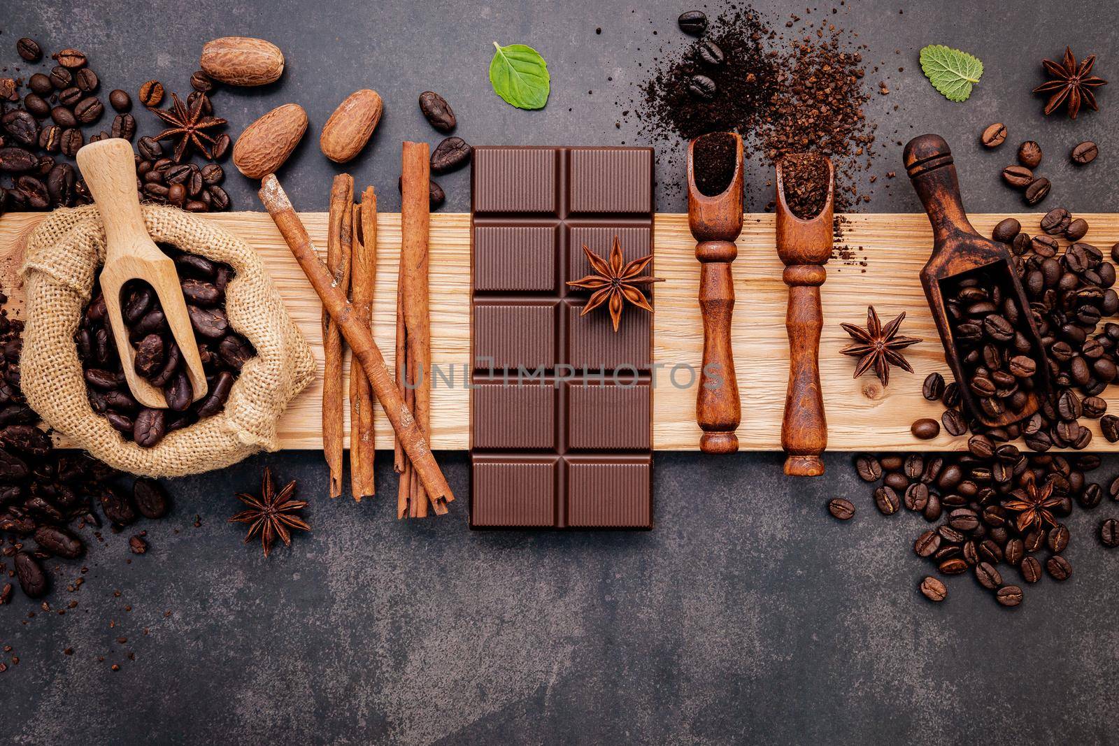 Roasted coffee beans with coffee powder and flavourful ingredients for make tasty coffee setup on dark stone background.