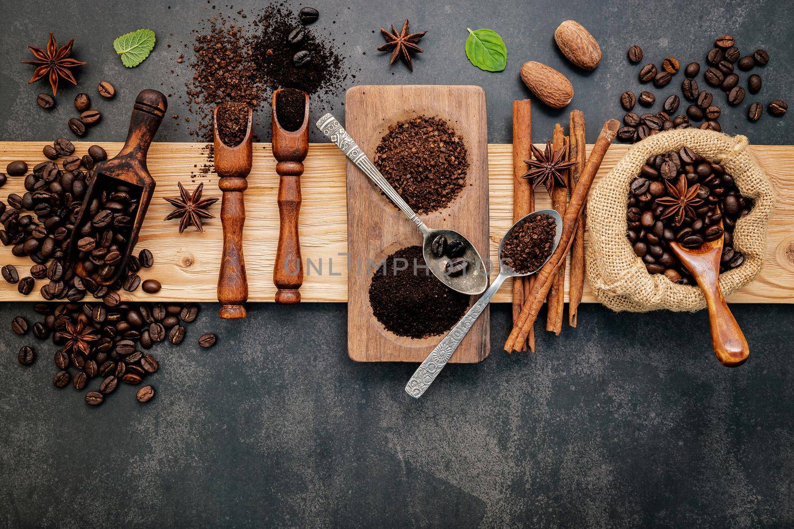 Roasted coffee beans with coffee powder and flavourful ingredients for make tasty coffee setup on dark stone background.