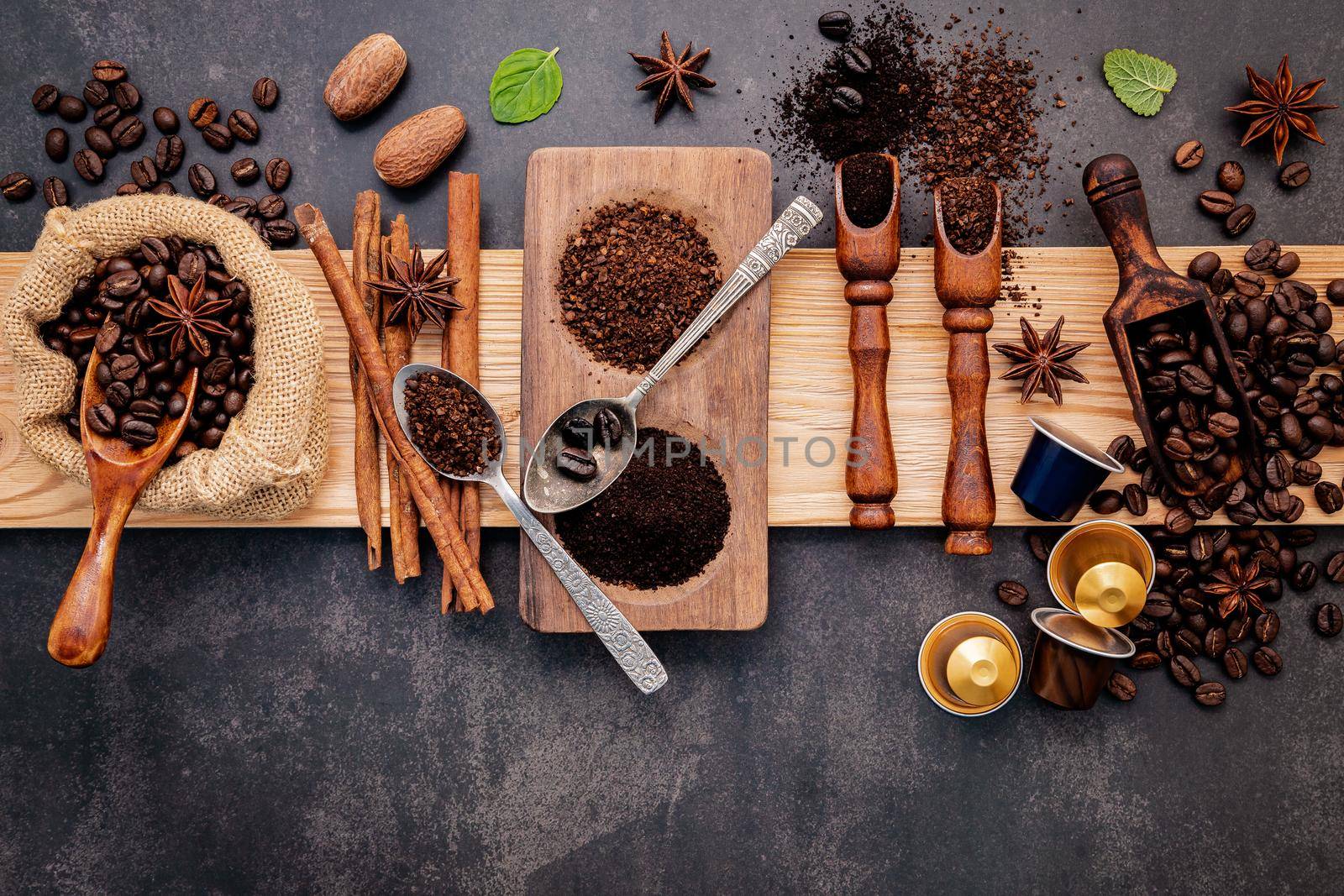 Roasted coffee beans with coffee powder and flavourful ingredients for make tasty coffee setup on dark stone background.