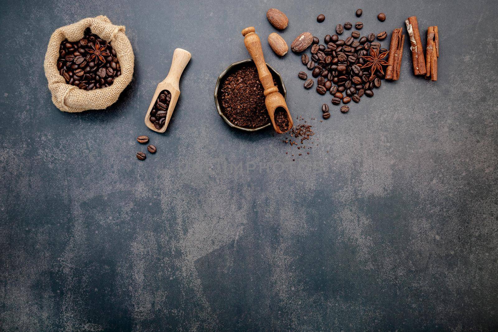 Roasted coffee beans with coffee powder and flavourful ingredients for make tasty coffee setup on dark stone background.