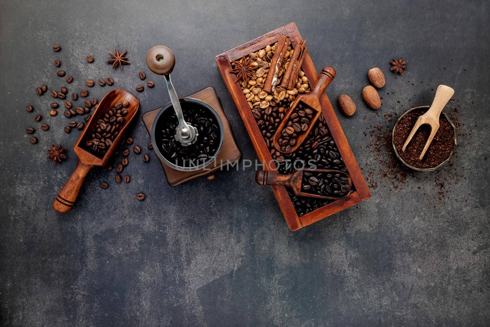 Various of roasted coffee beans in wooden box with manual coffee grinder setup on dark stone background.