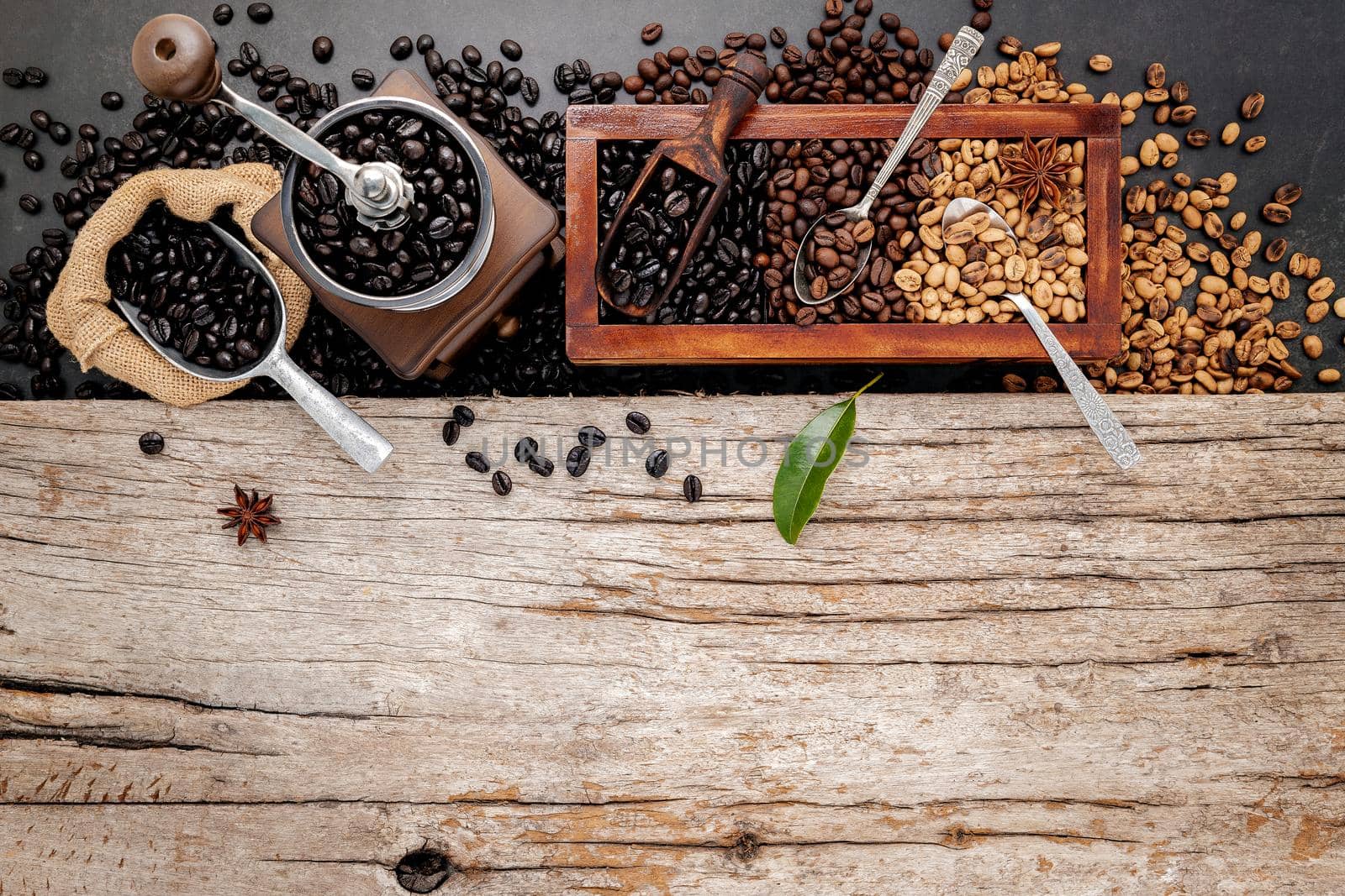 Various of roasted coffee beans in wooden box with manual coffee grinder setup on shabby wooden background.