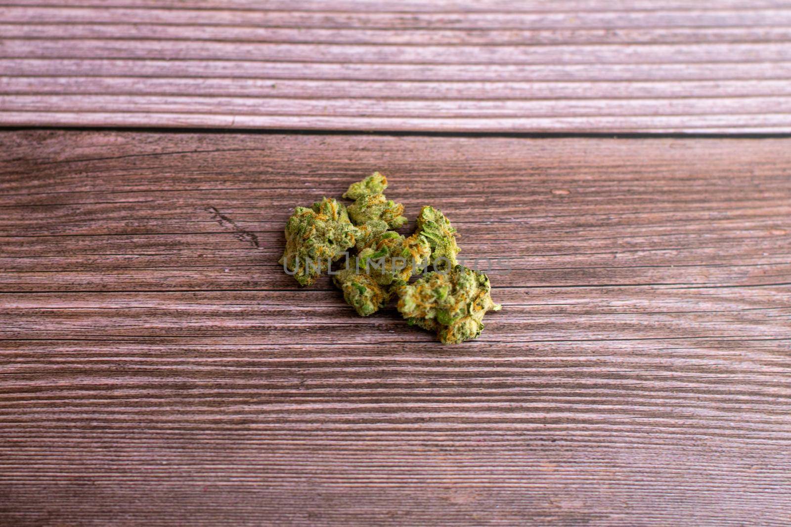 A Small Pile of Bright Green and Orange Medicinal Cannabis on a Brown Wooden Background