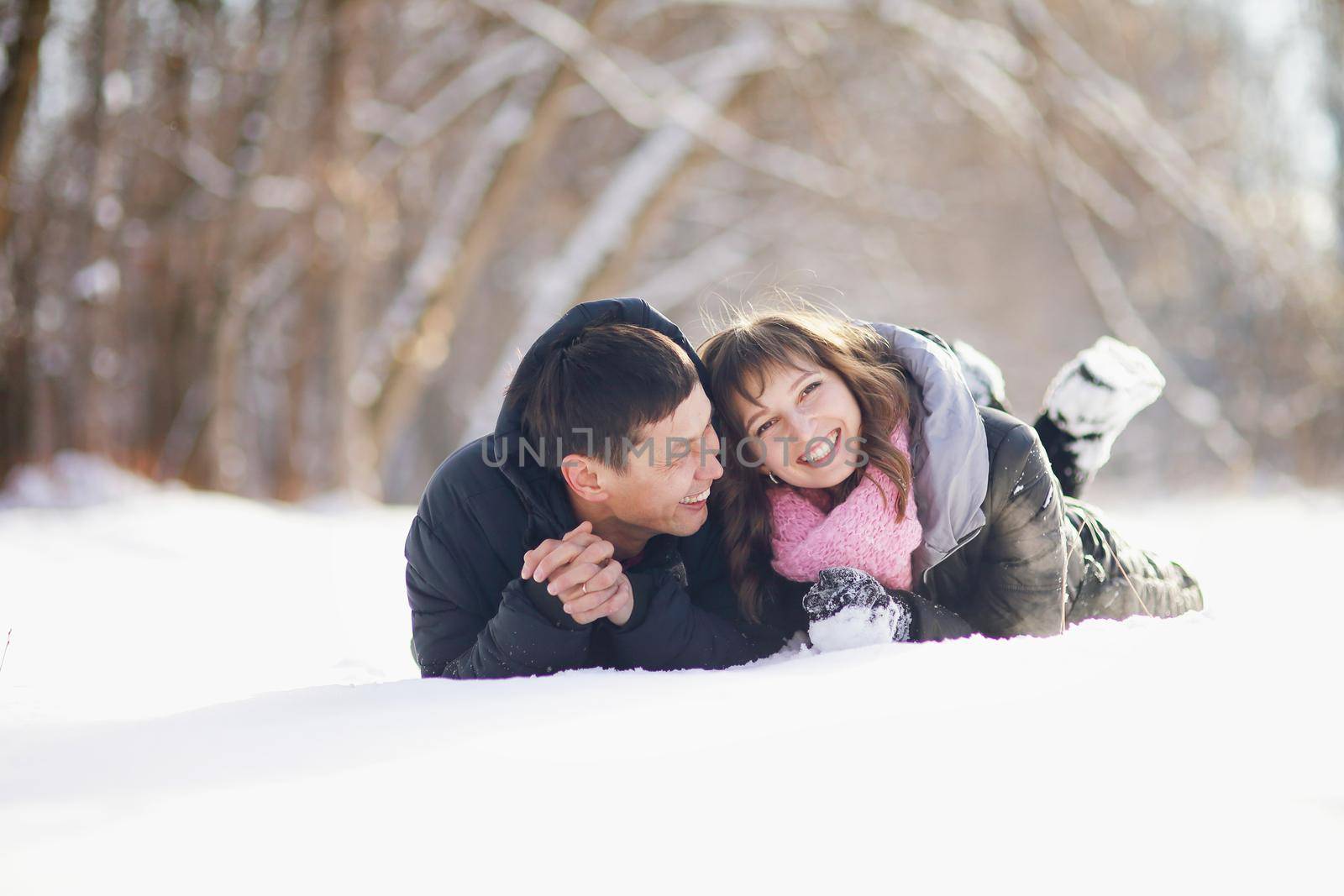 Happy couple lying on the snow and laughing. 