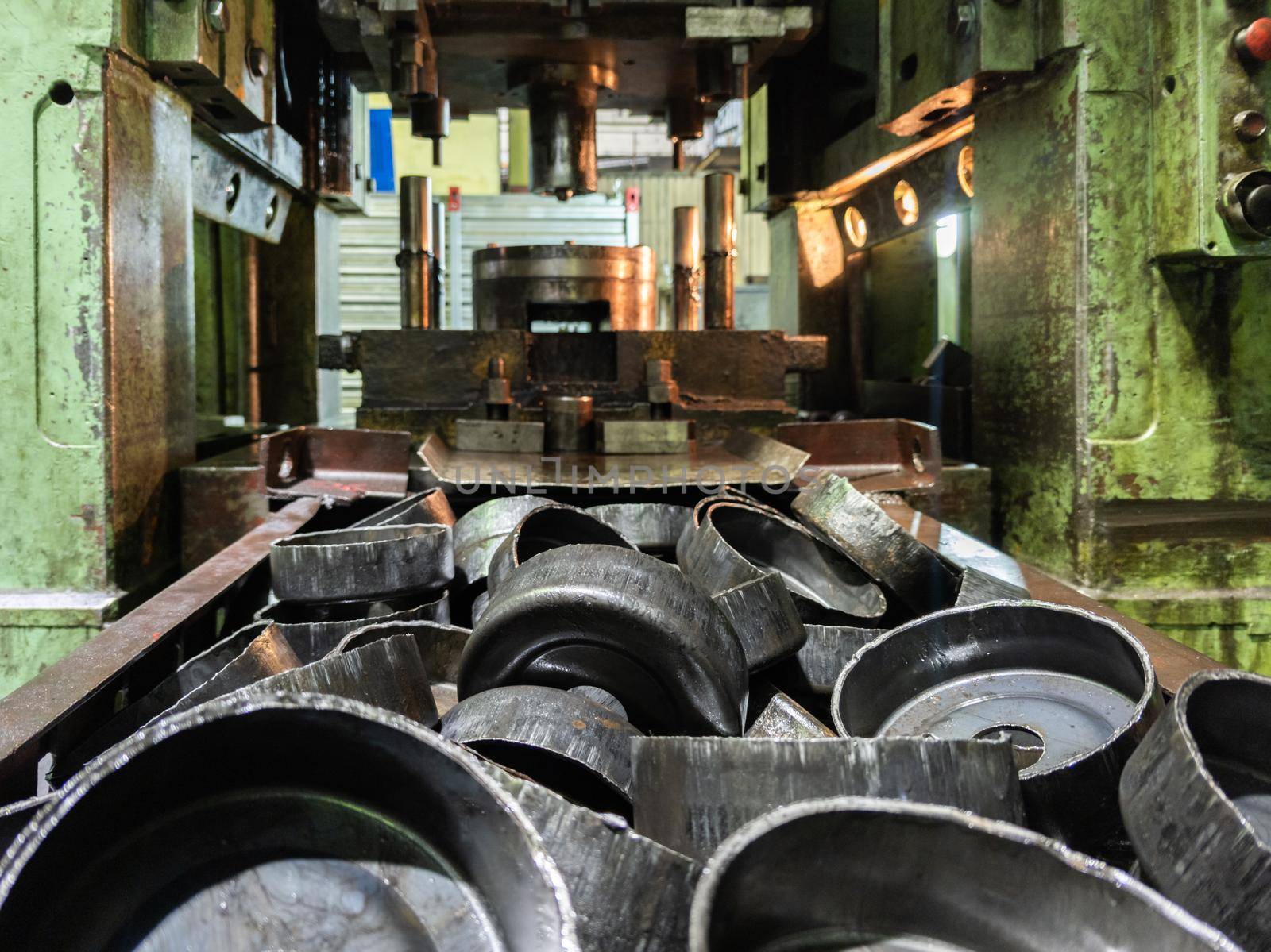 pile of stamped thick sheet black metal round parts after a hood operation in front of old blurred forming press with die tooling