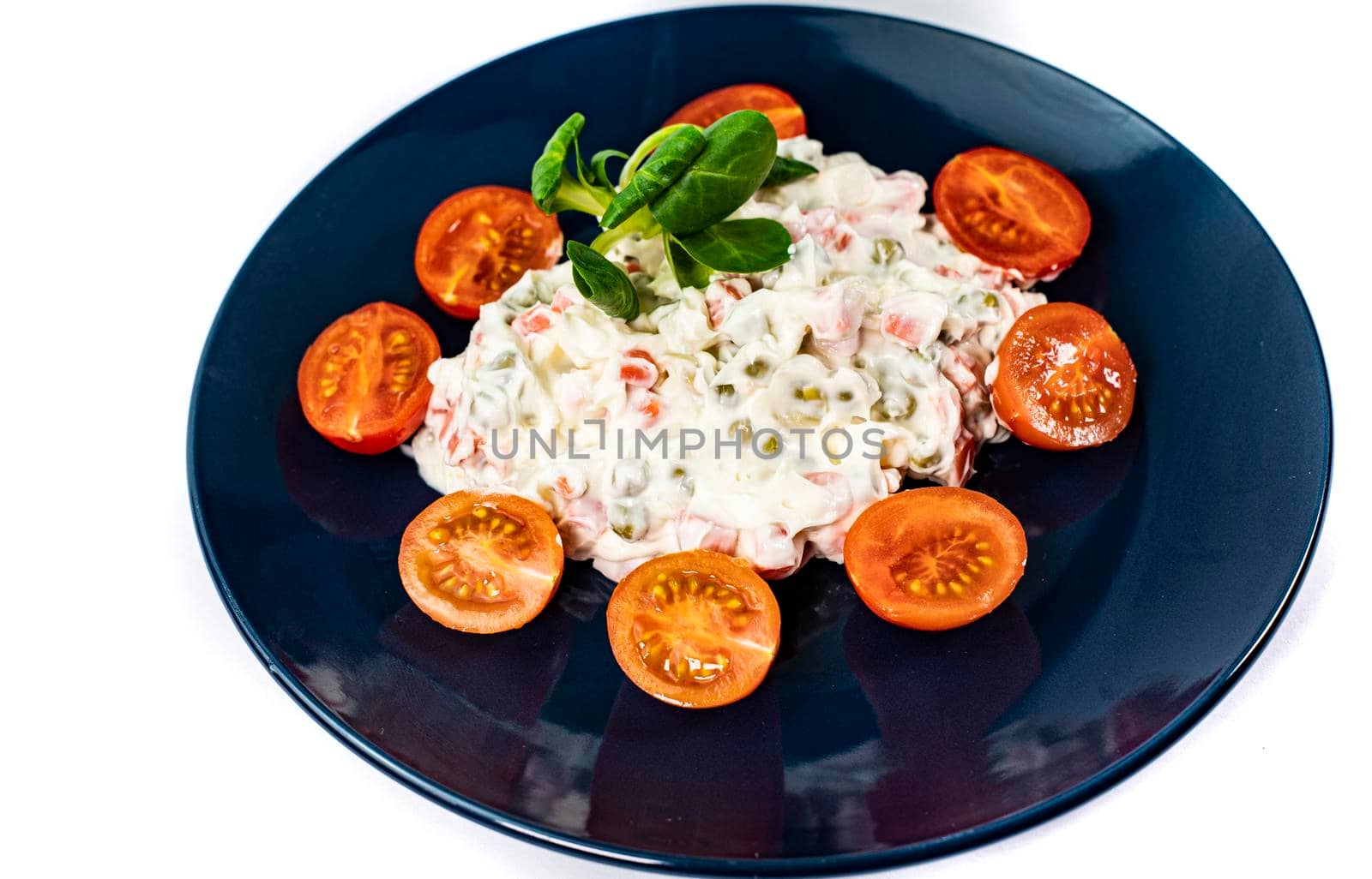 Russian salad on blue plate with cherry tomatoes on white background