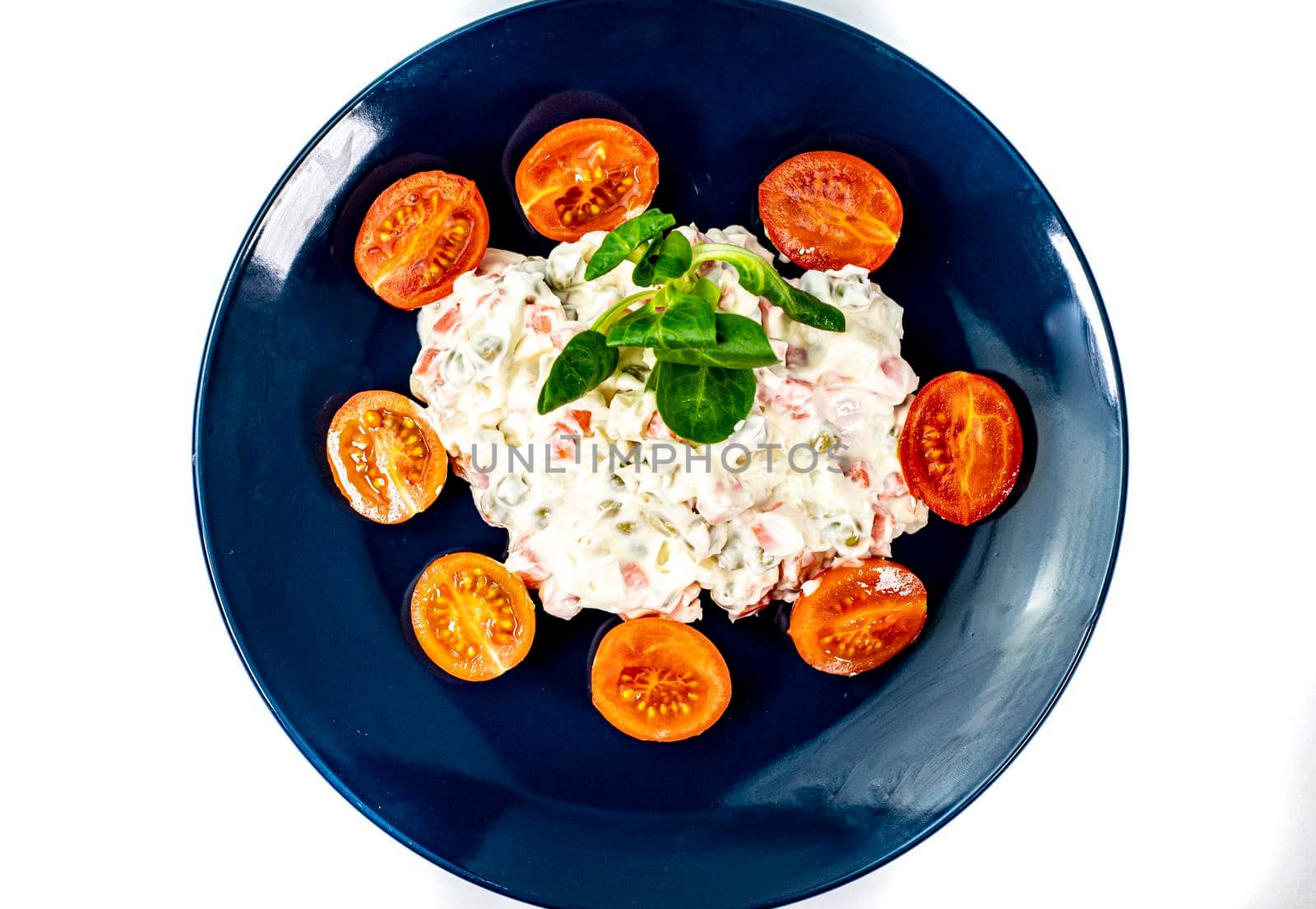 Russian salad on blue plate with cherry tomatoes on white background