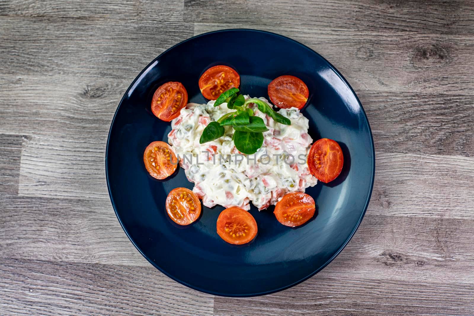 Russian salad in blue plate with cherry tomatoes on wooden background