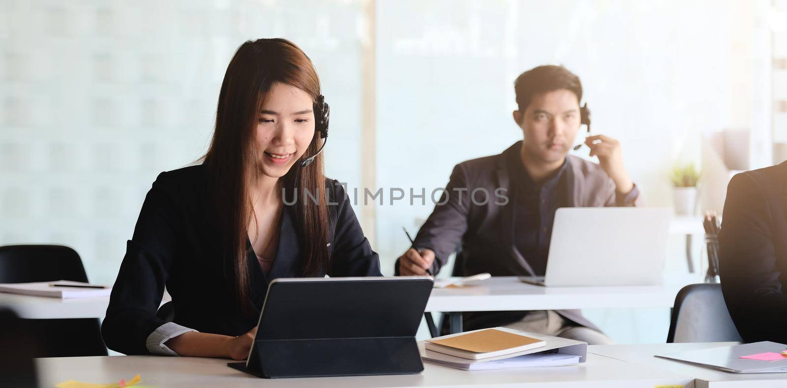 Young asian woman working in call centre, surrounded by colleagues. by nateemee