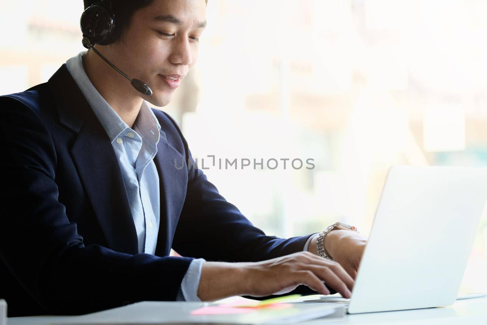Asian businessman in headphones looking at laptop, watching good webinar, consulting client, distance learning languages, making notes, happy man participating online conference. by nateemee