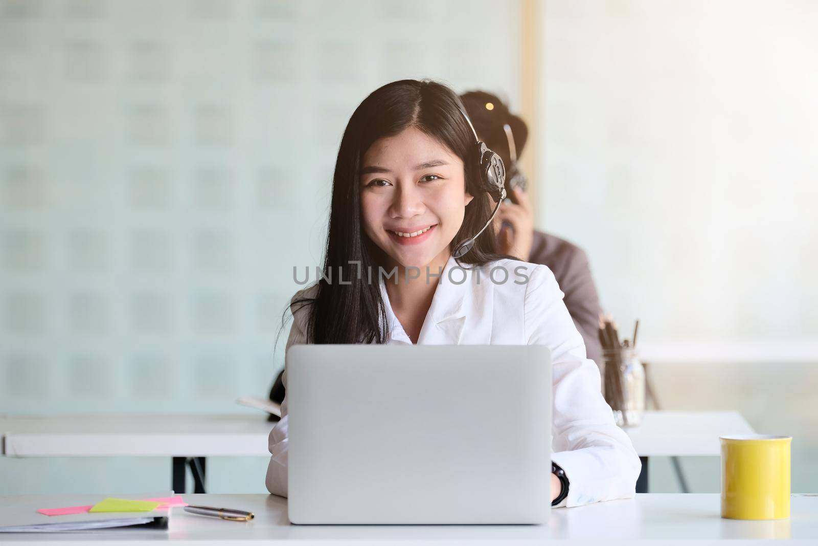 Portrait of young asian woman working in call centre, surrounded by colleagues