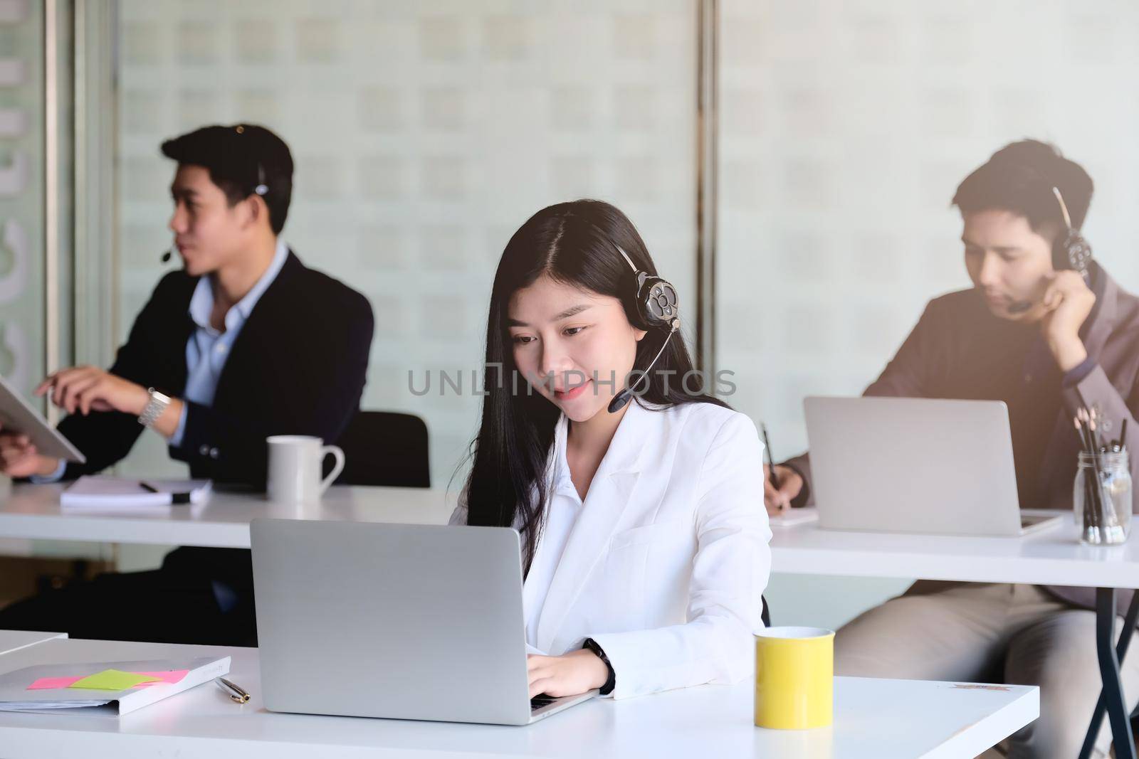 Young asian woman working in call centre, surrounded by colleagues