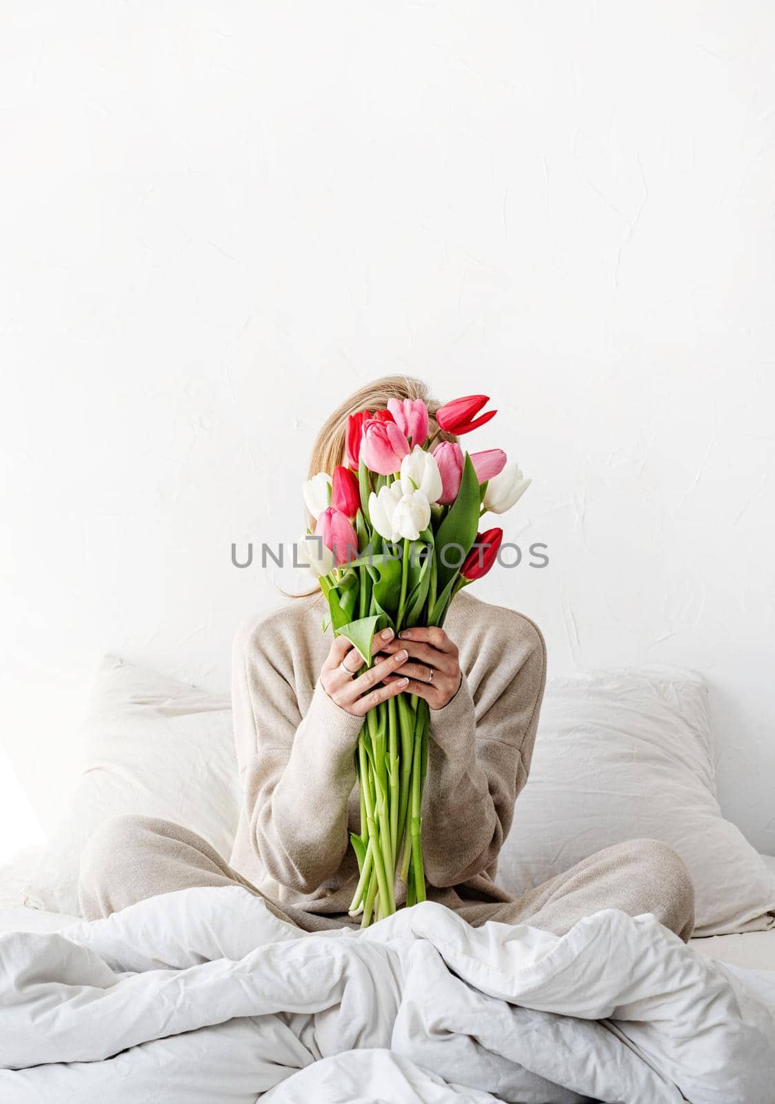 Happy woman sitting on the bed wearing pajamas, with pleasure enjoying flowers