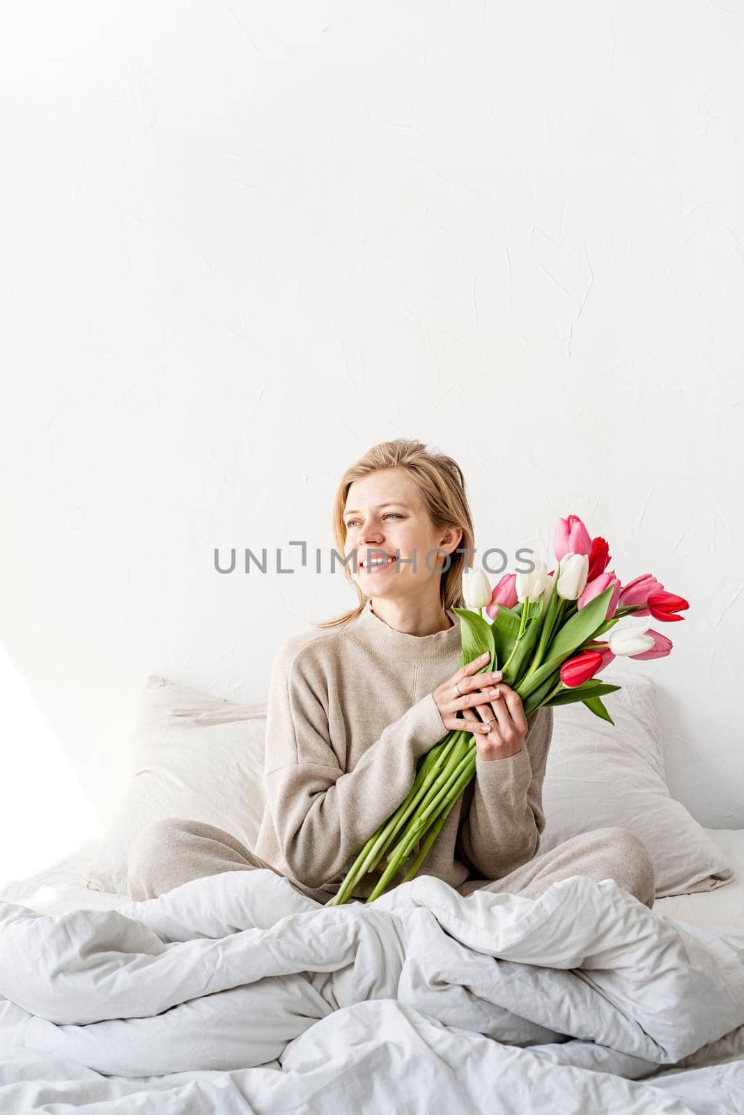 Happy woman sitting on the bed wearing pajamas, with pleasure enjoying flowers