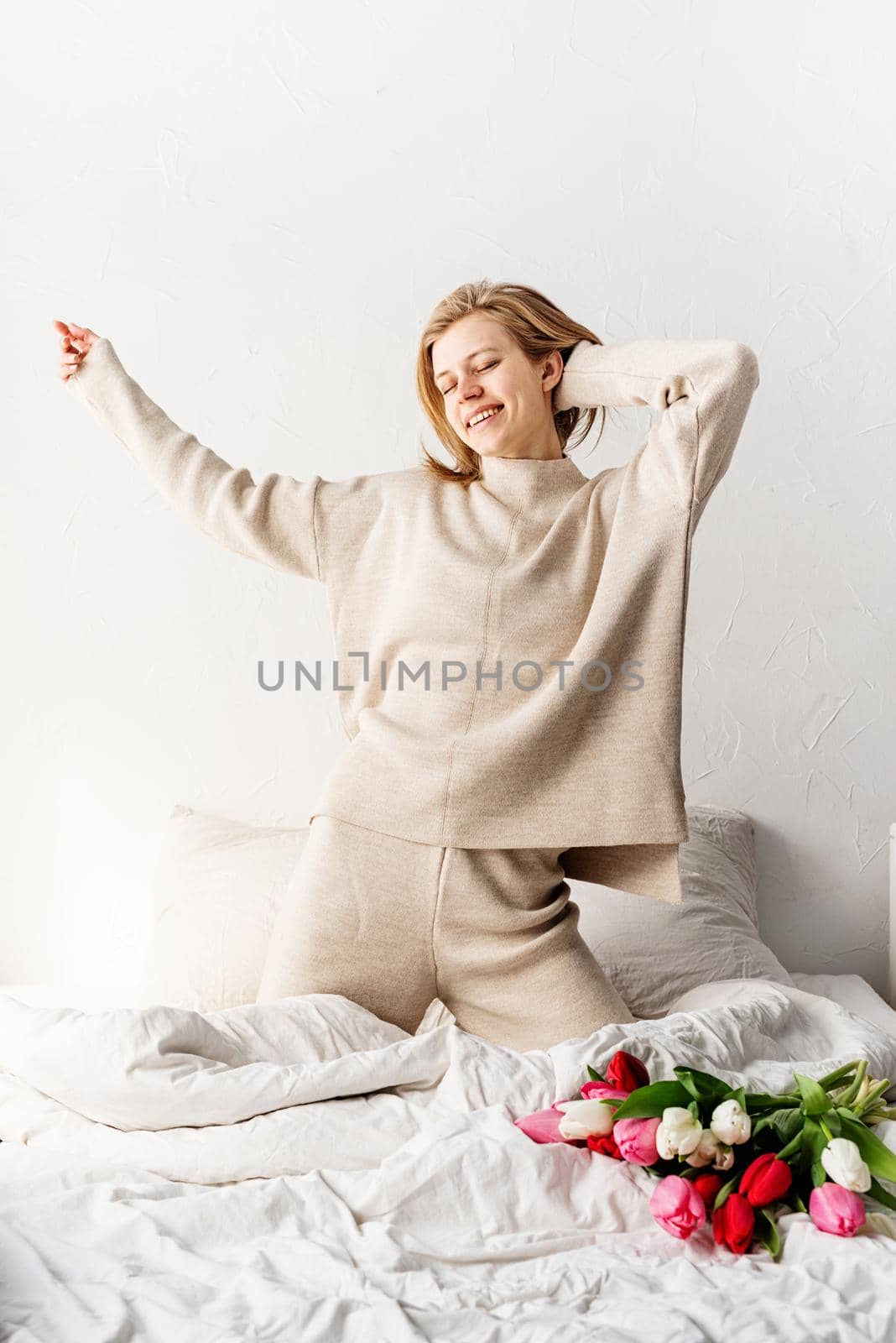 Happy young woman wearing pajamas dancing on the bed having fun