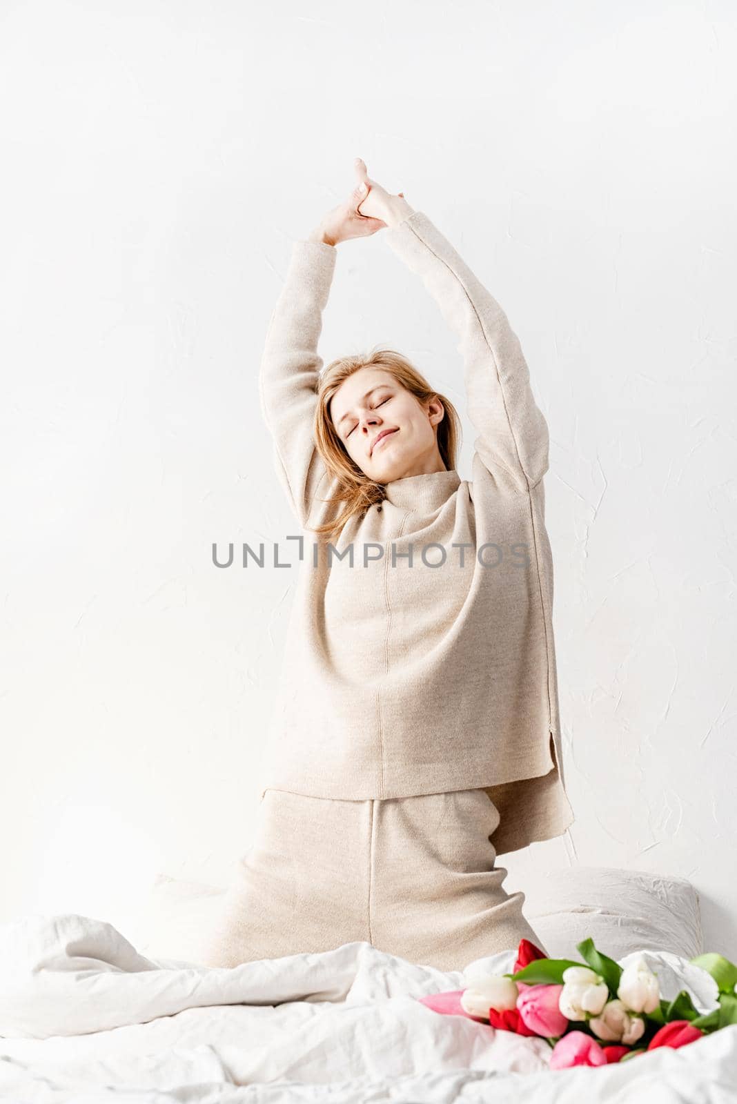 Smiling young woman wearing pajamas stretching on the bed in the morning