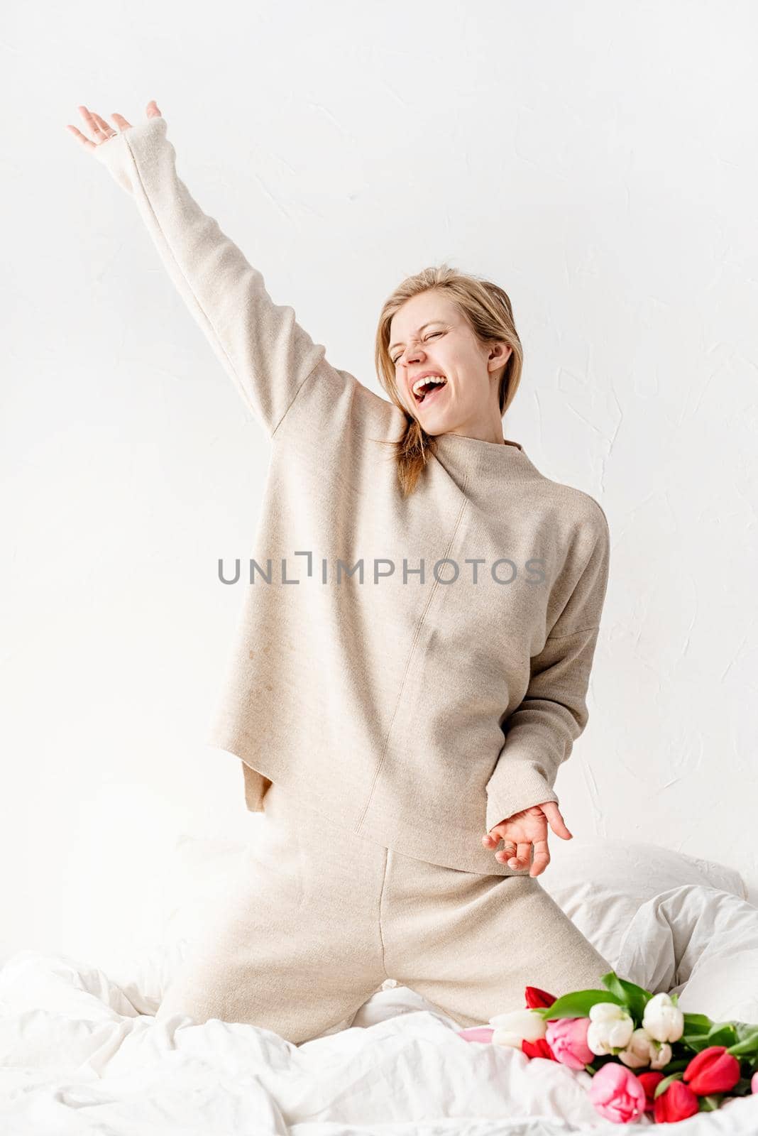 Happy young woman wearing pajamas dancing on the bed by Desperada