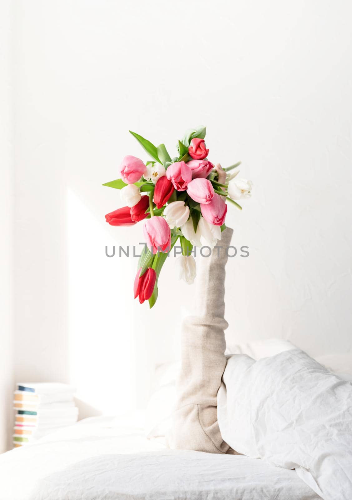 Woman arm outstreched from the blanket holding a bouquet of tulip flowers. Woman in bed holding tulip flowers