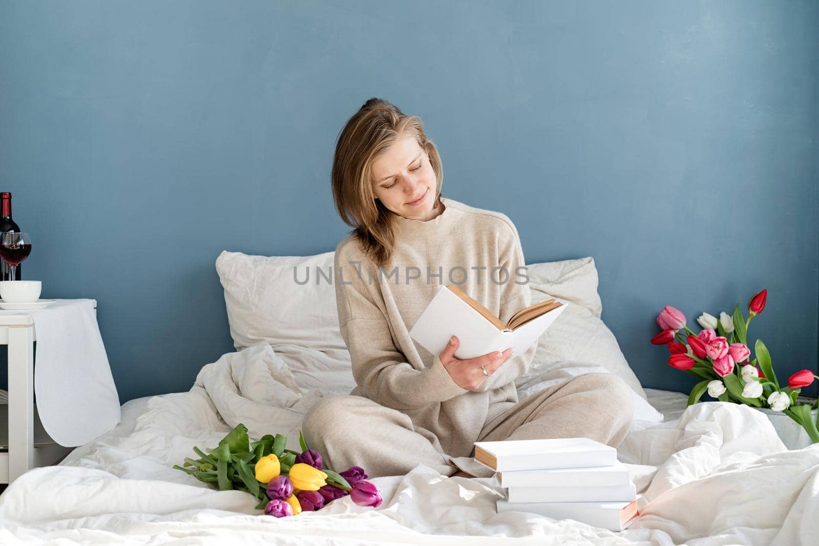 Happy woman sitting on the bed wearing pajamas reading a book by Desperada