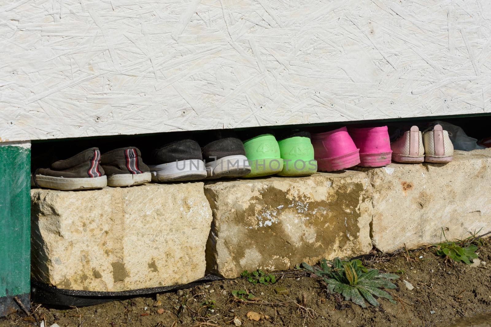 Under the house in the garden there is a row of various shoes