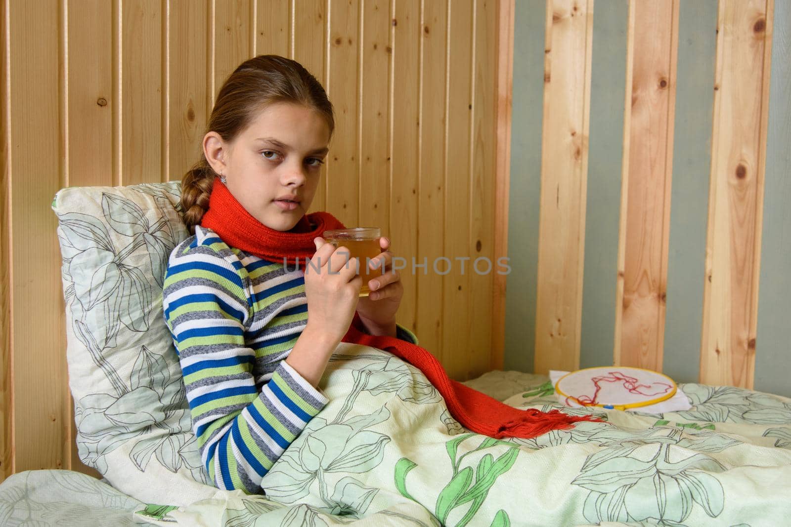 Sick girl drinking tea while sitting in bed, the girl looked into the frame